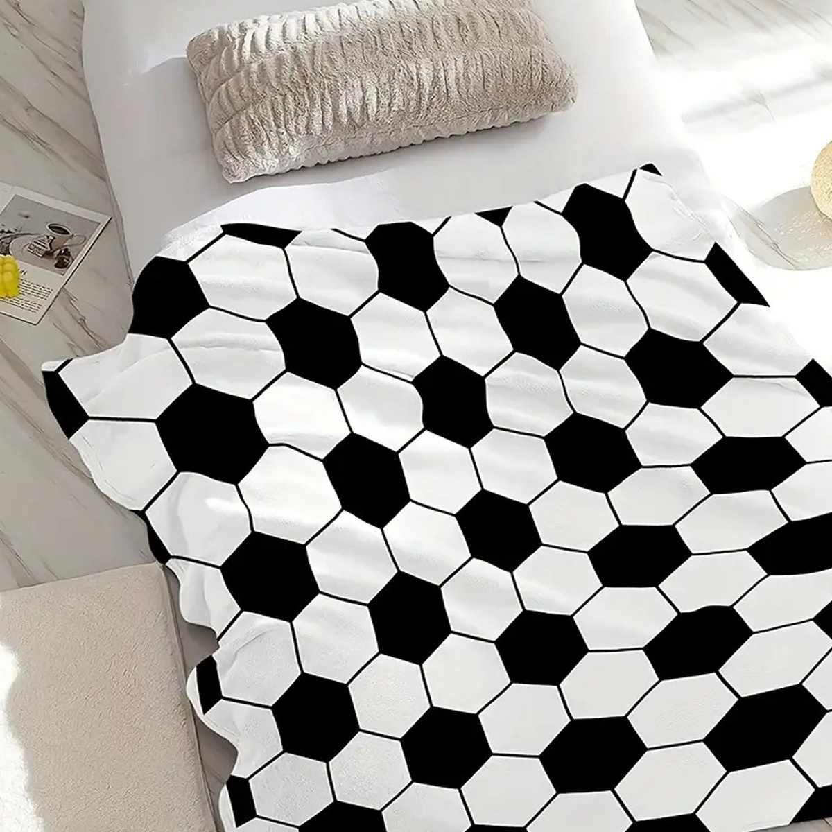 Decke mit einem schwarz-weißen Fußballmuster auf einem weißen Bett.