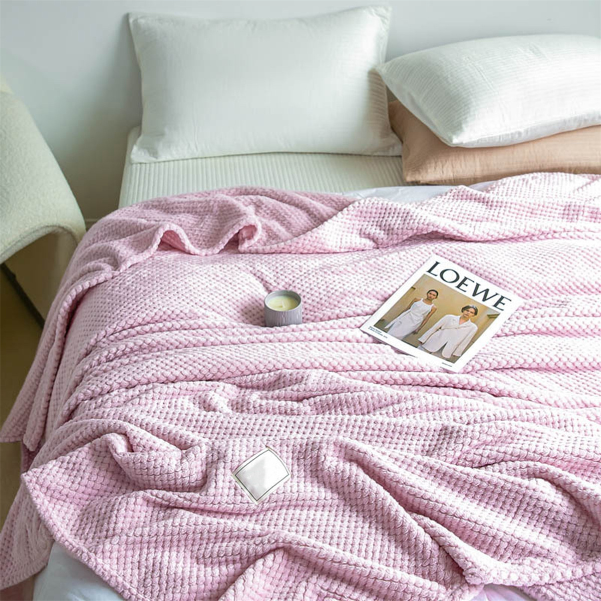 Ein Bett mit einer rosa Decke, Kissen und einer Zeitschrift, das eine gemütliche Szene schafft.