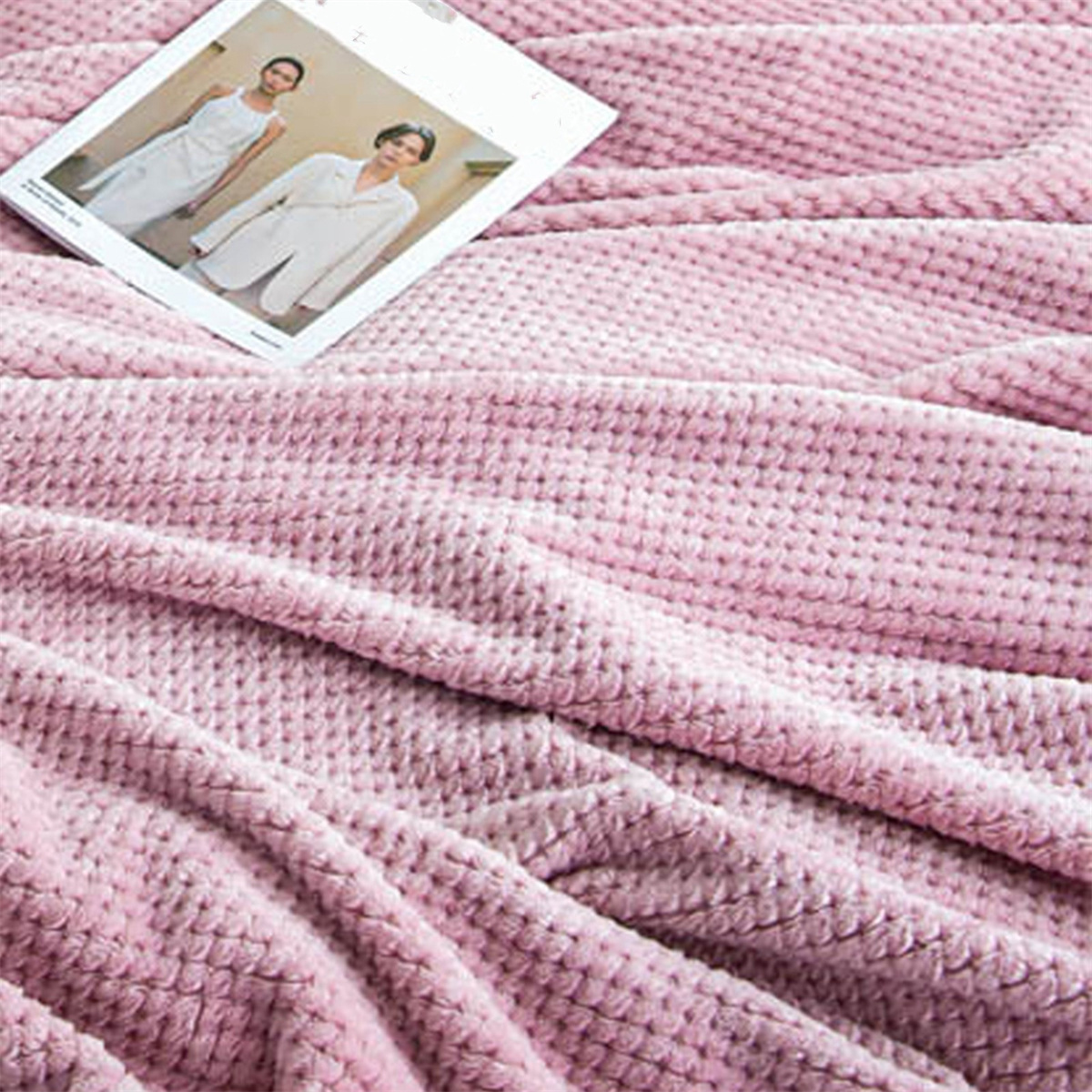Rosa, strukturierte Decke mit einer Zeitschrift obenauf, die zwei Frauen in weißer Kleidung zeigt.