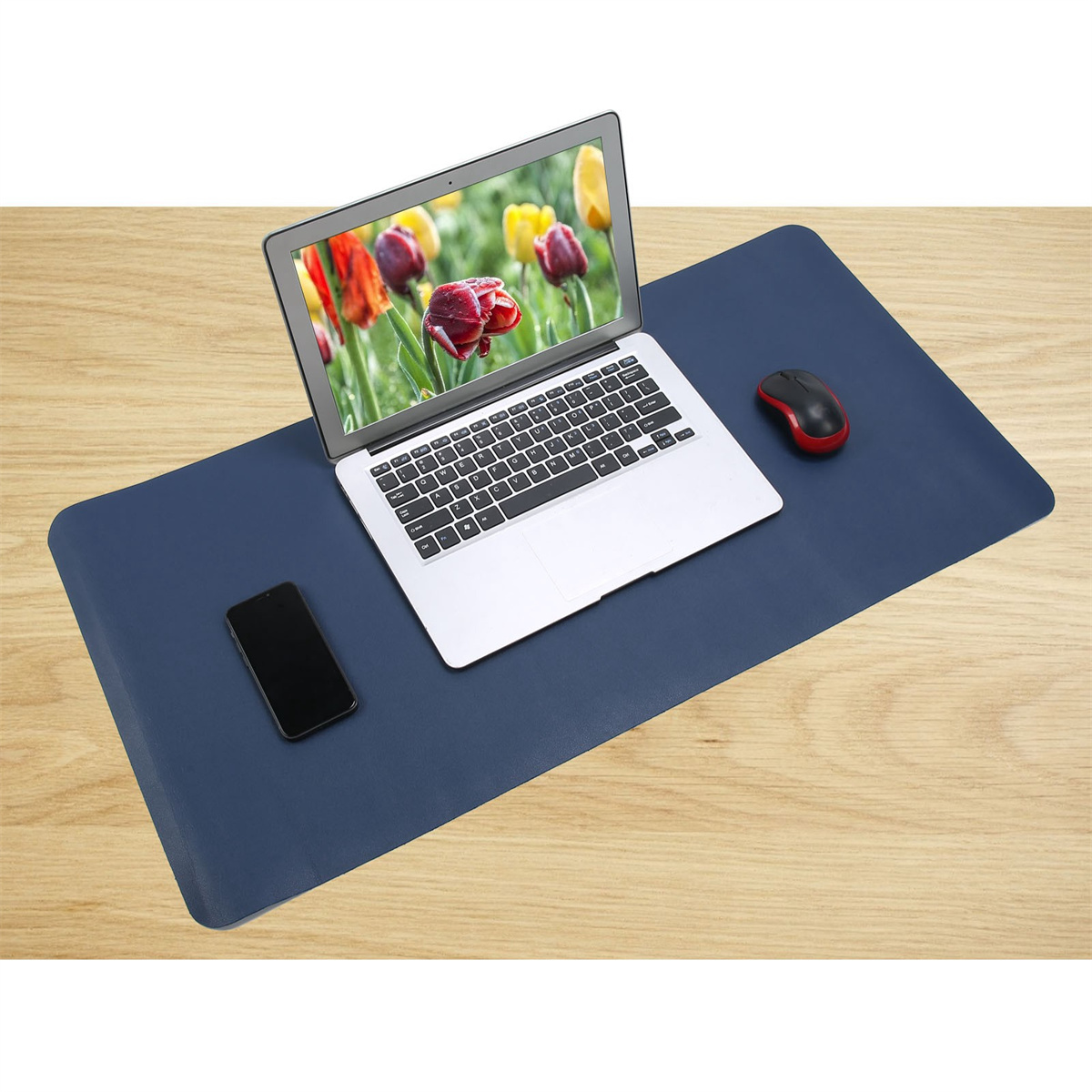 Laptop mit roten Tulpen, Maus und Telefon auf einer blauen Schreibtischunterlage auf einem Holztisch.