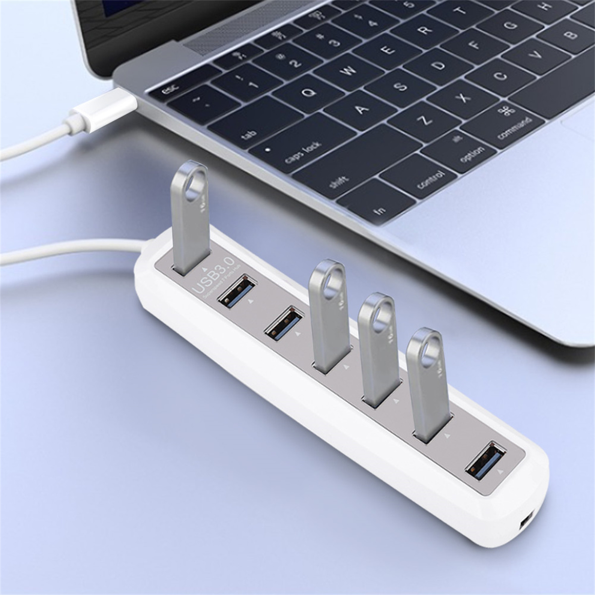 Ein weißer USB-Hub, der mit einem Laptop verbunden ist. Vier USB-Laufwerke sind an den Hub angeschlossen.
