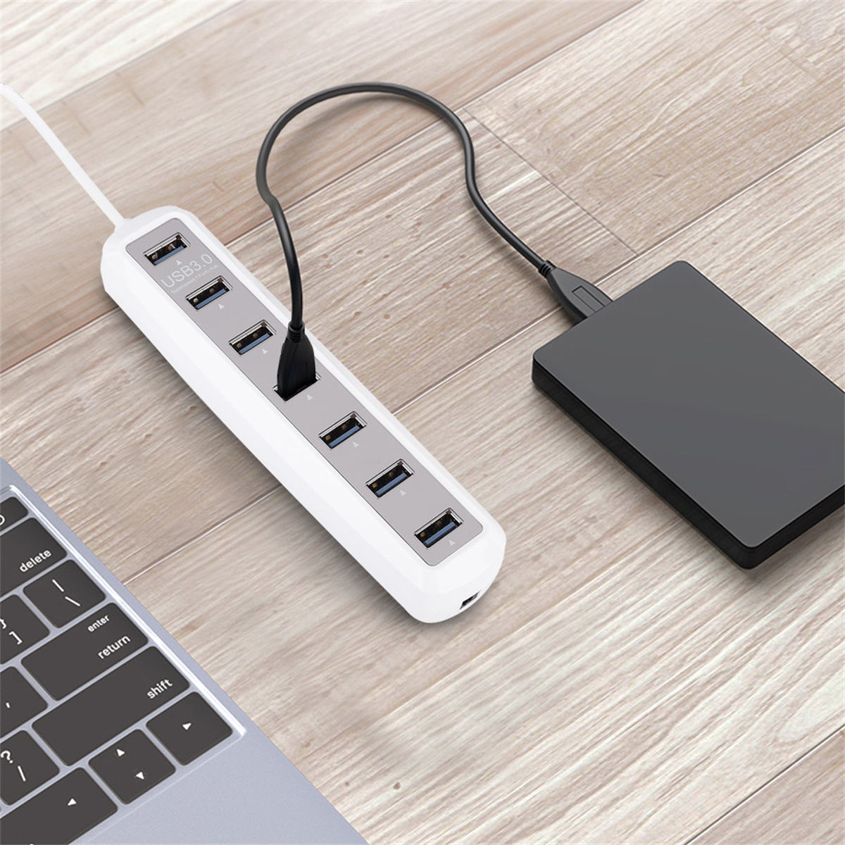 Ein weißer USB-Hub mit einem schwarzen Kabel, das an eine schwarze externe Festplatte auf einer Holzoberfläche angeschlossen ist.
