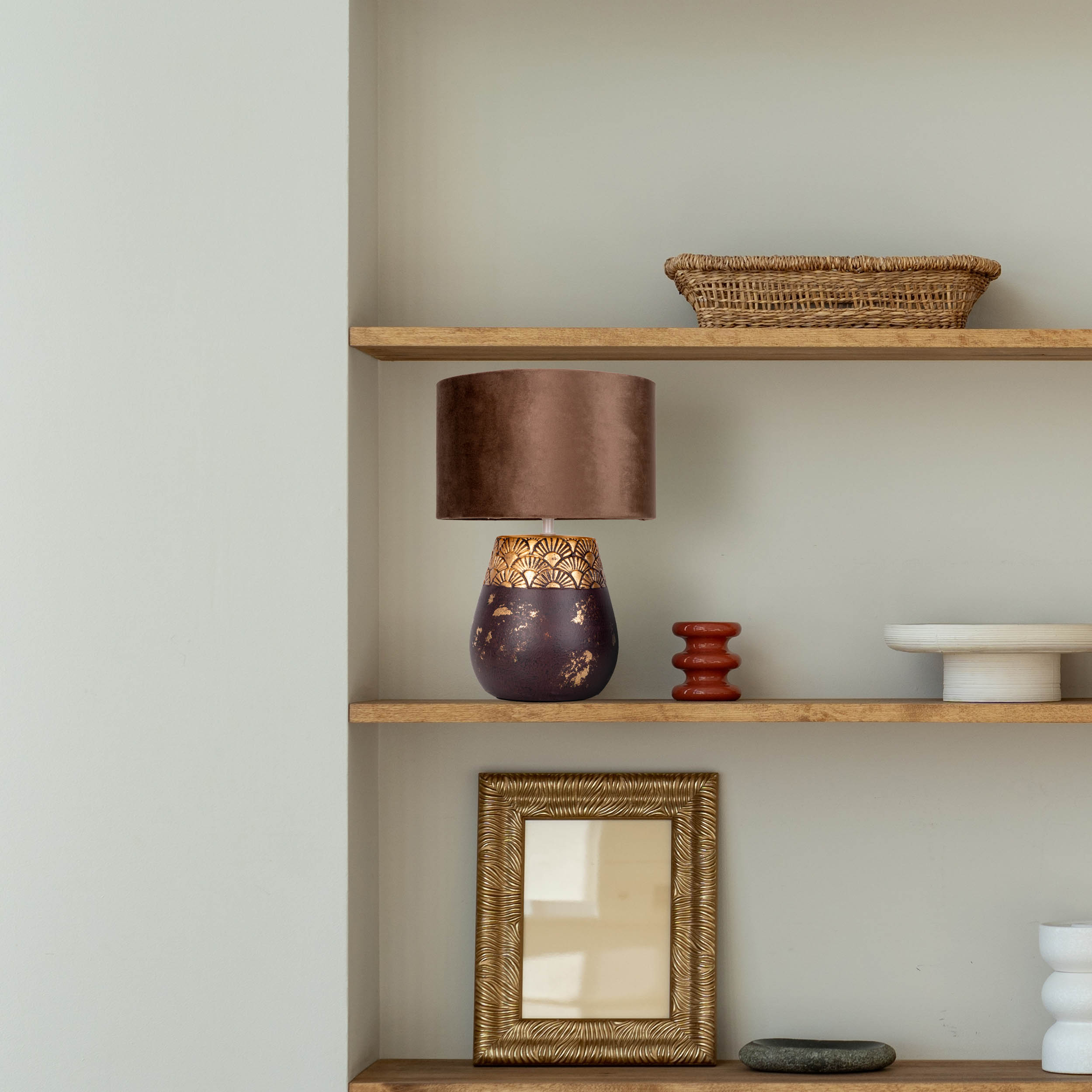 Bücherregal mit Lampe, Spiegel und anderen Dekorationsgegenständen. Die Lampe hat einen braunen Schirm.