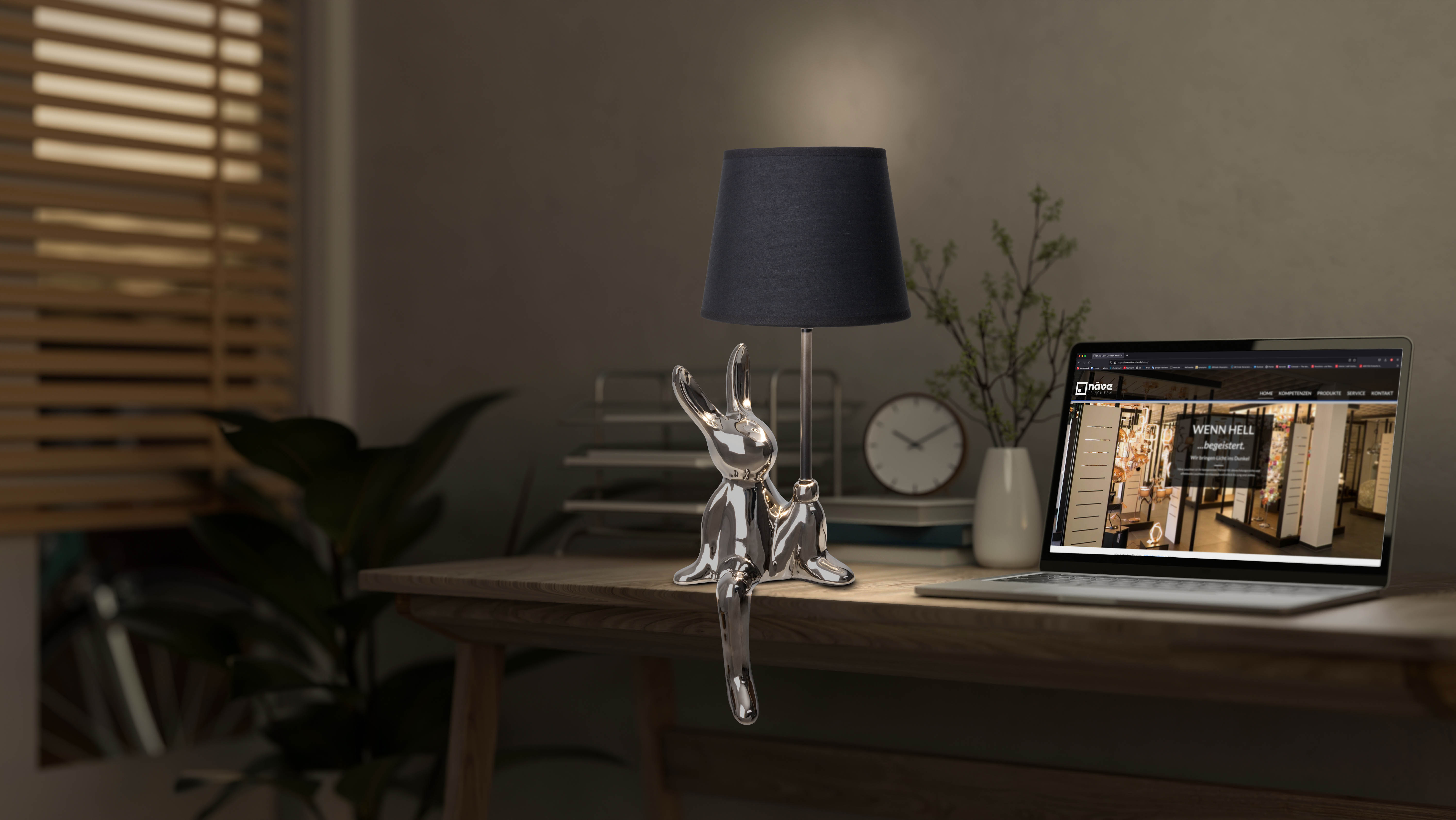 Eine Glas-Kaninchen-Lampe und ein Laptop auf einem Holzschreibtisch.