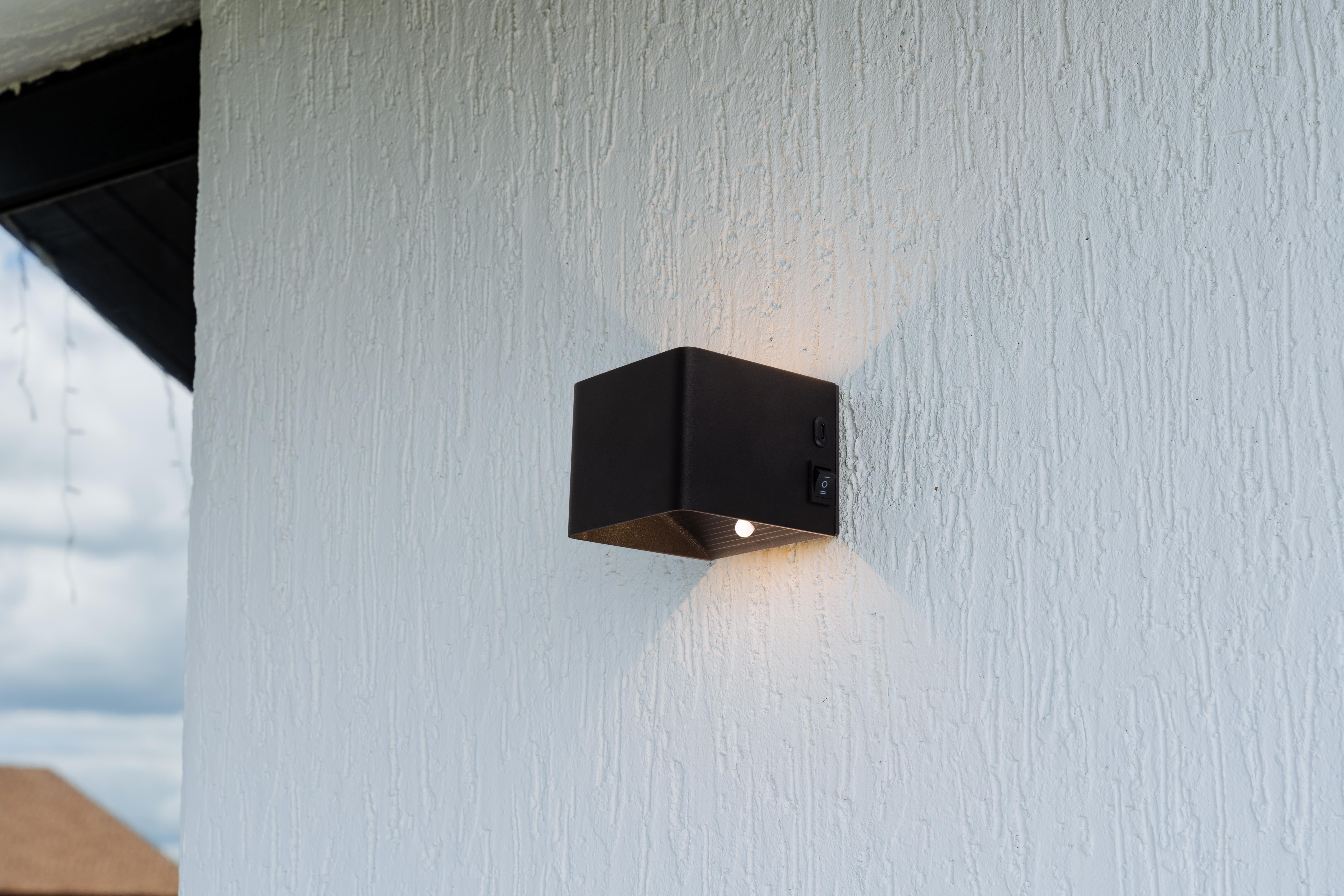 Eine schwarze Außenleuchte an einer strukturierten weißen Wand. Es hat einen Schalter.