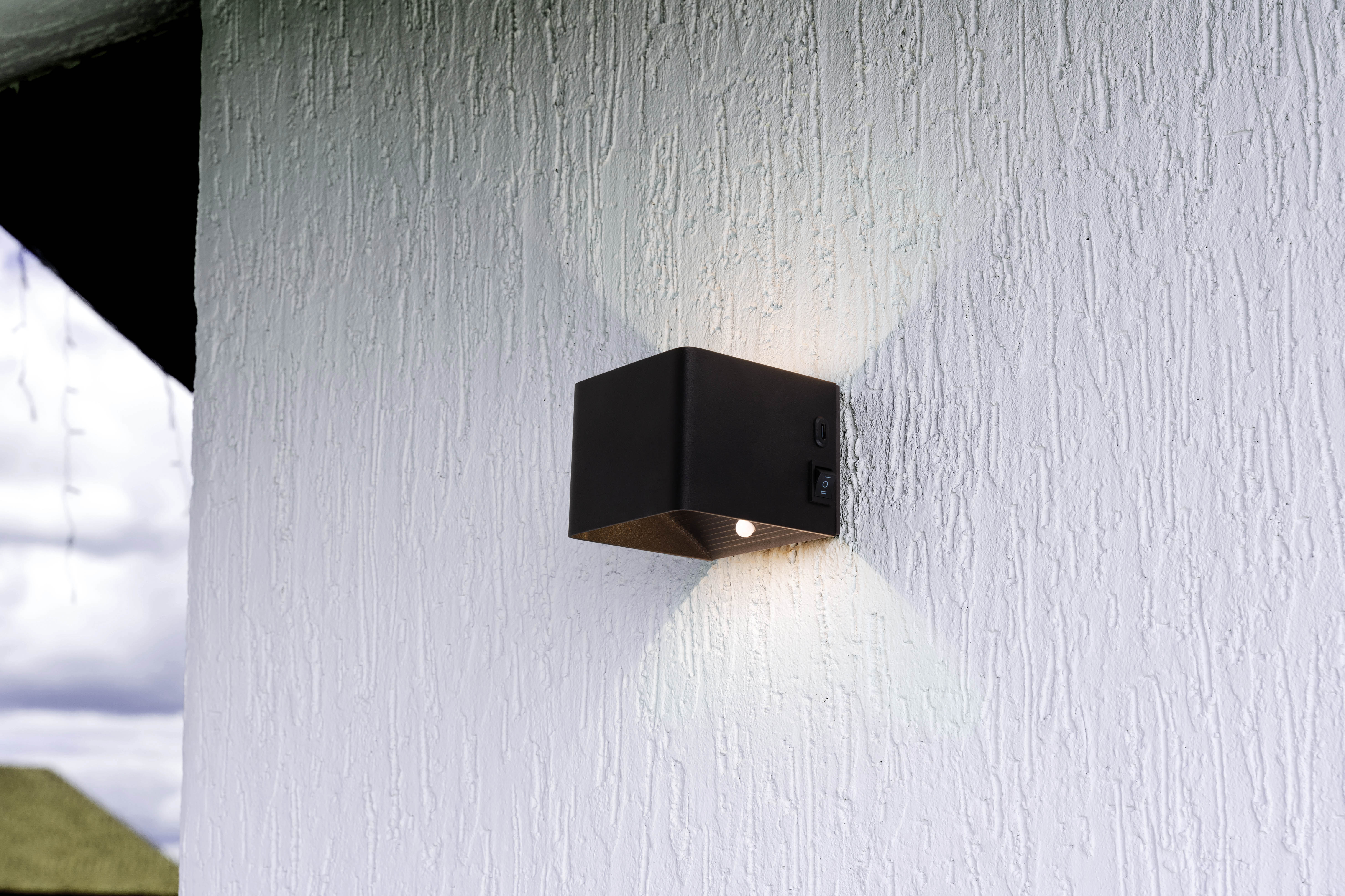 Schwarze quadratische Außenwandleuchte an strukturierter weißer Wand mit Schalter.