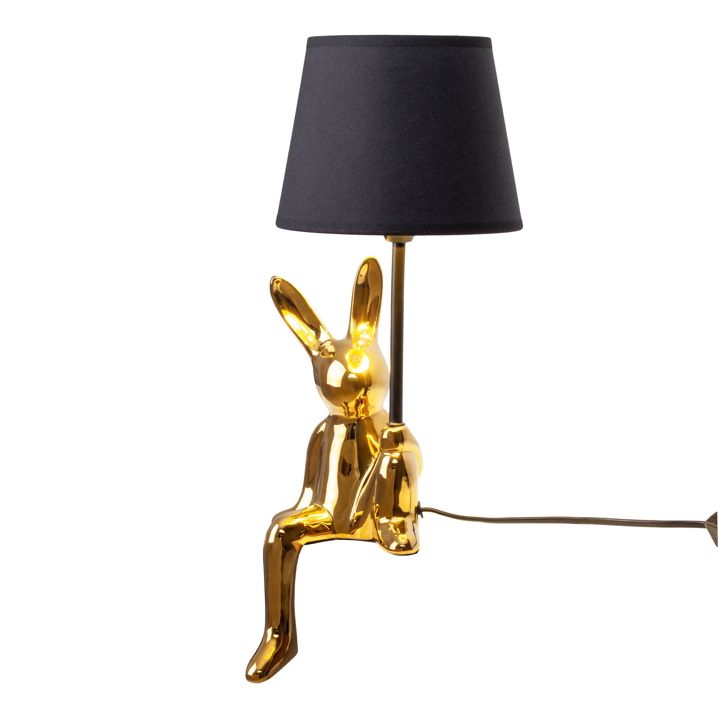 Eine goldene Hasenlampe mit schwarzem Lampenschirm. Der Hase sitzt und hält die Lampe.