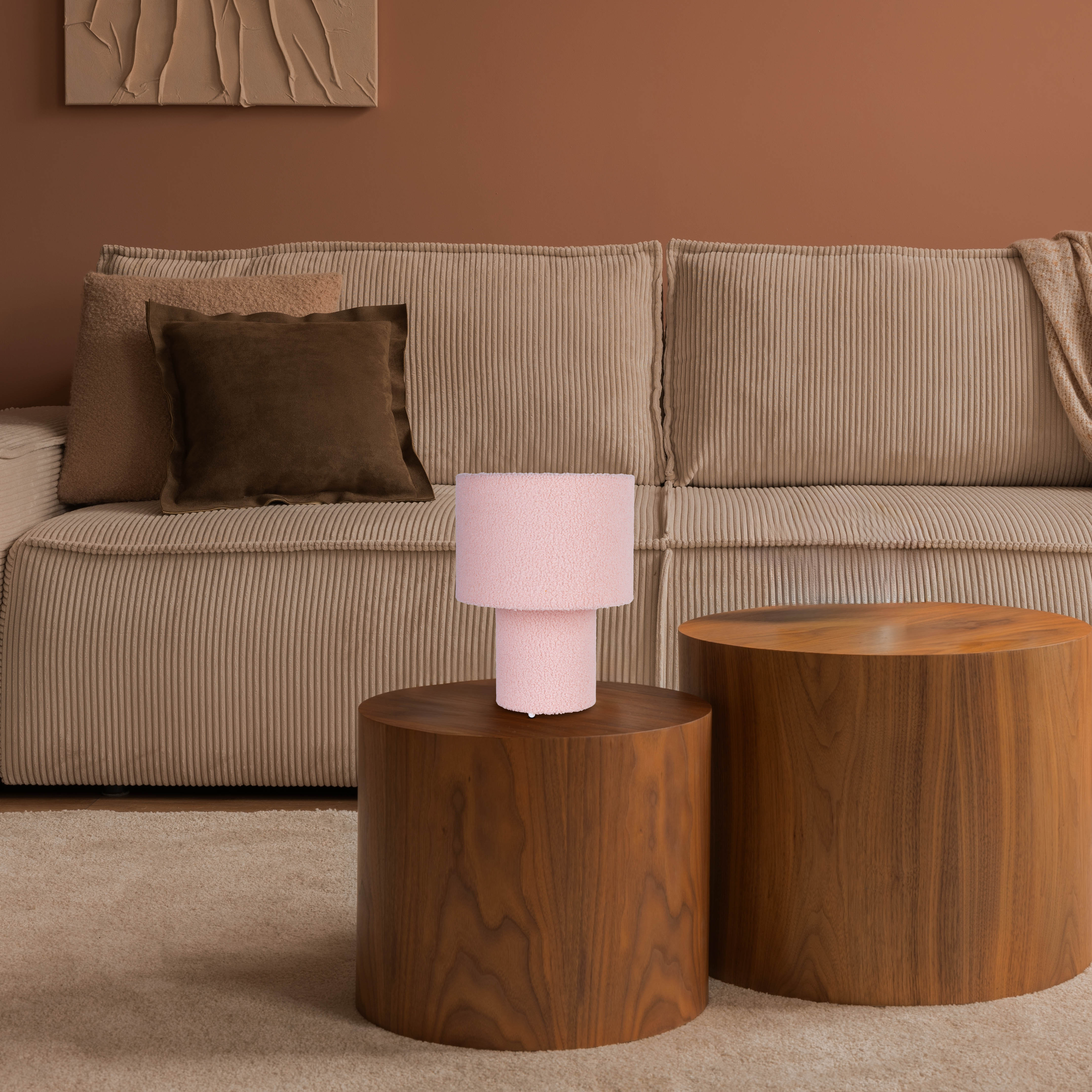 Beiges Cordsofa mit braunen Kissen. Pinkfarbene Lampe auf einem Holztisch. Daneben ein weiterer Holztisch.