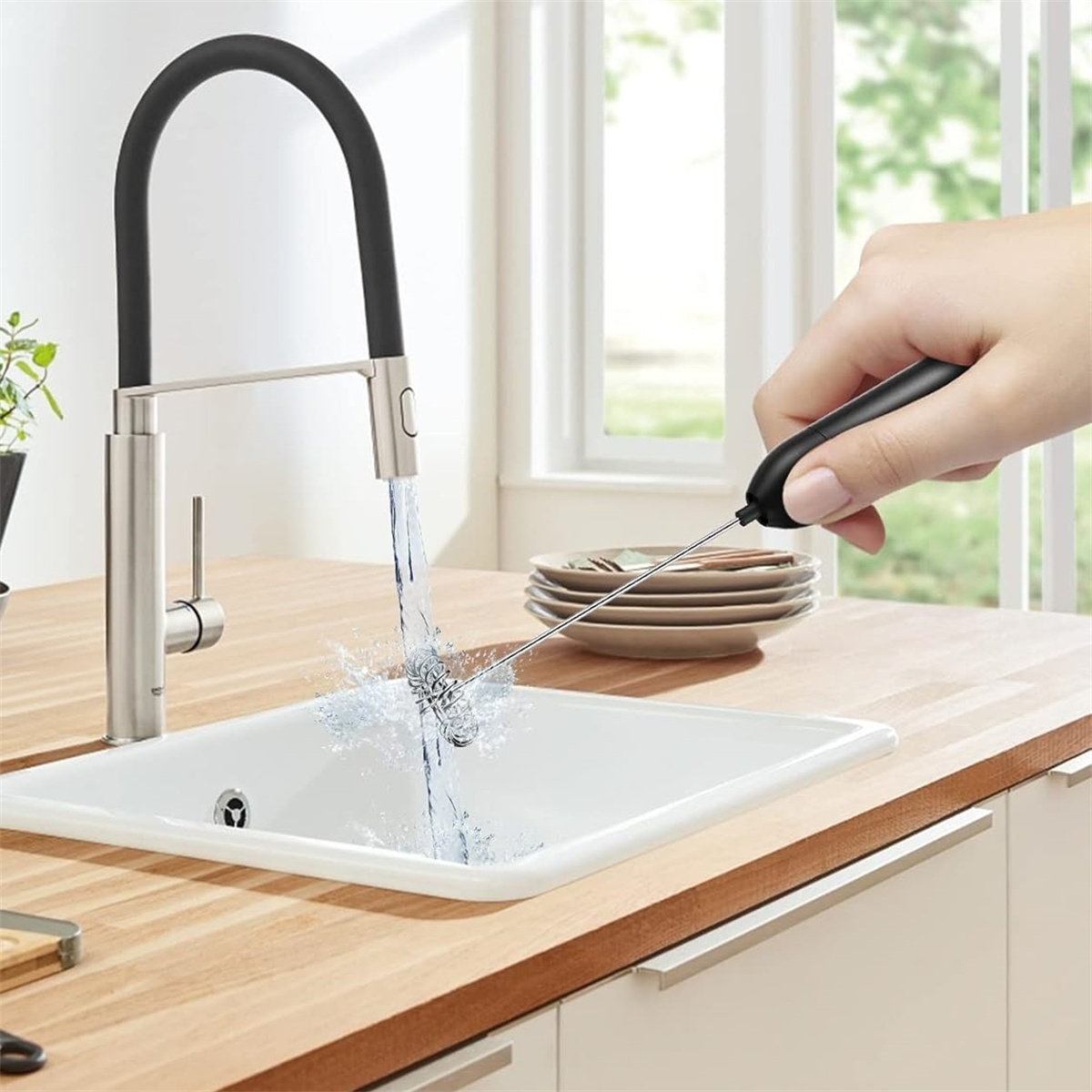 Ein Waschbecken mit einem schwarzen Wasserhahn und einer Hand, die einen Schneebesen hält, Wasser spritzt.