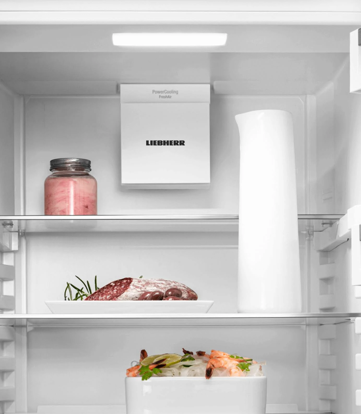 Dentro de un refrigerador con alimentos en los estantes. Tarro y plato con comida.