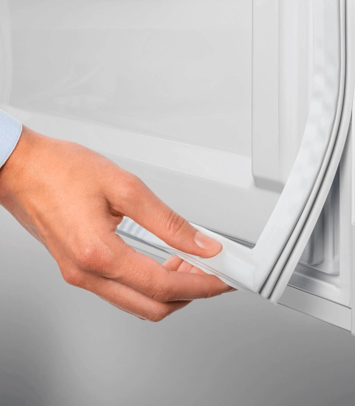 La mano de una persona sosteniendo el sello de goma de la puerta de un refrigerador. El sello es blanco.