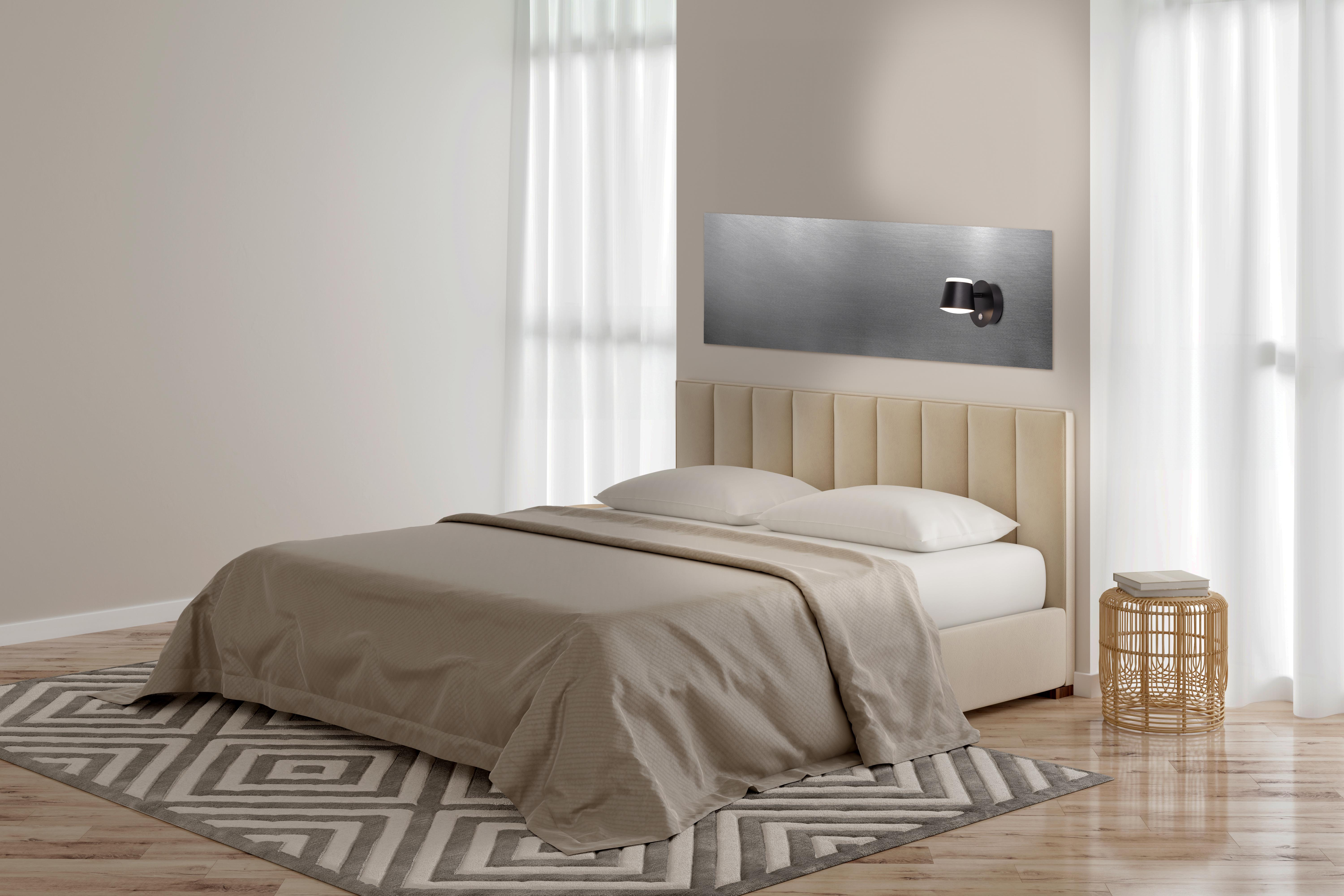 Ein beiges Bett in einem Schlafzimmer mit zwei Kissen und einer Decke. Es gibt Vorhänge und einen Teppich. Ein Bild an der Wand.