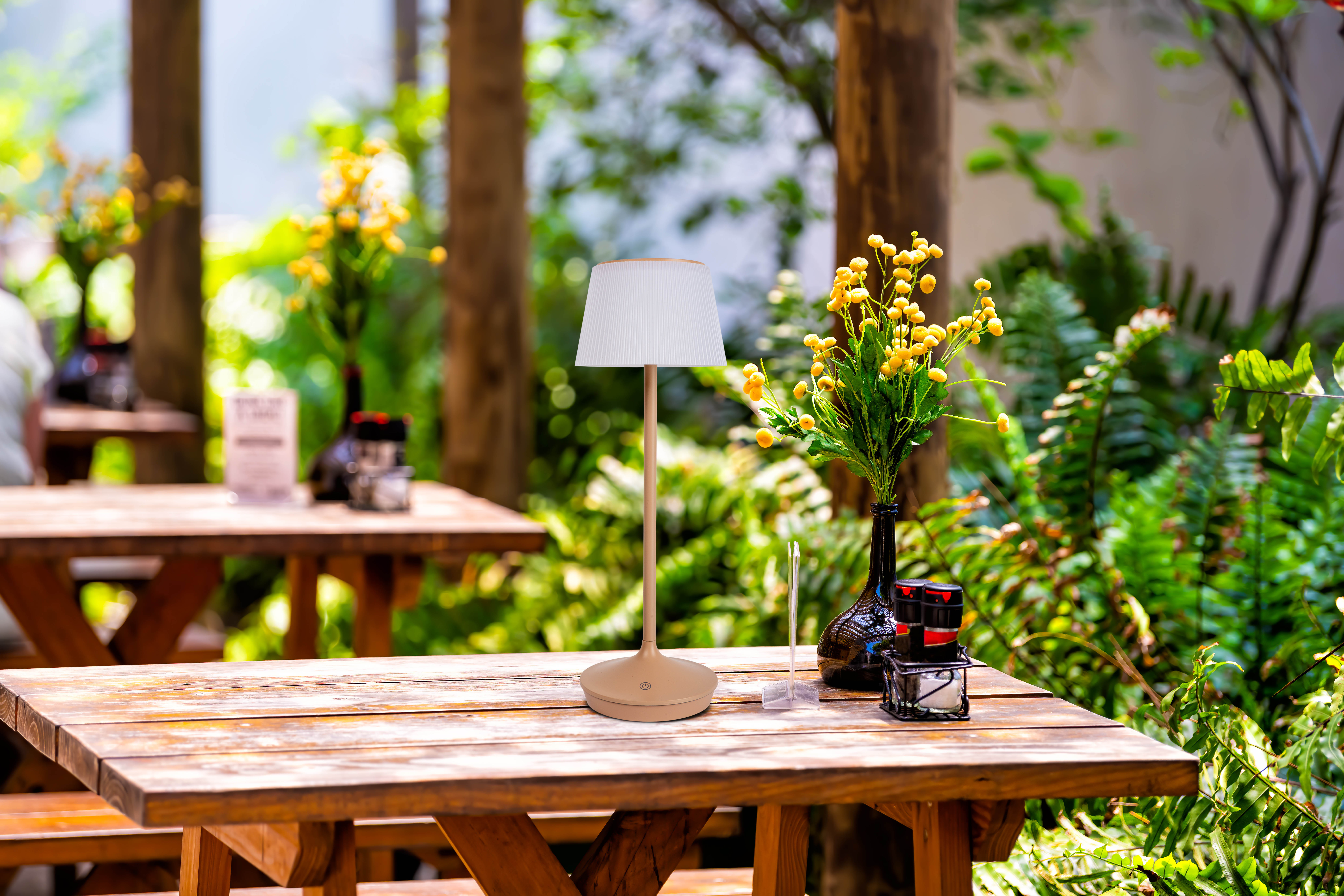 Tisch im Freien mit Lampe, Blumen und Holztischen. Grün im Hintergrund.