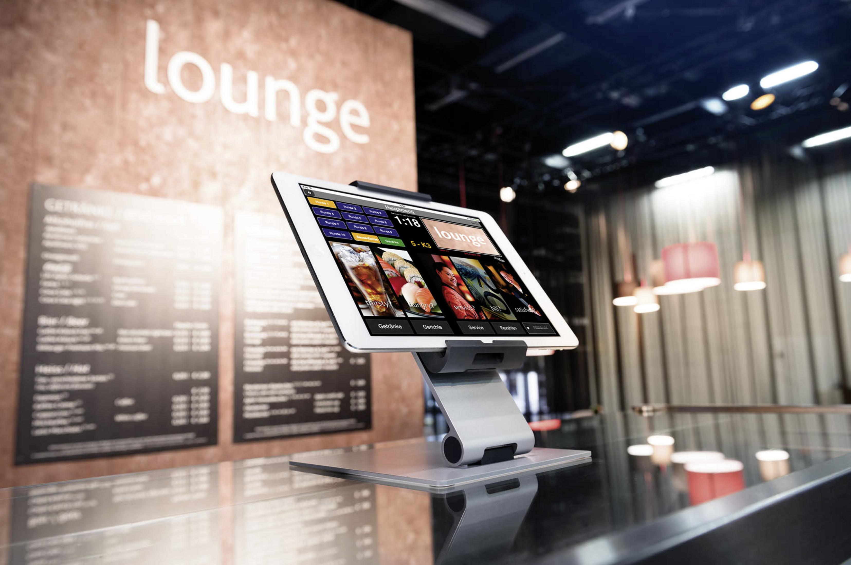 Tablet auf einem Ständer mit Menü, in einer Lounge mit Menütafel und anderen Personen.