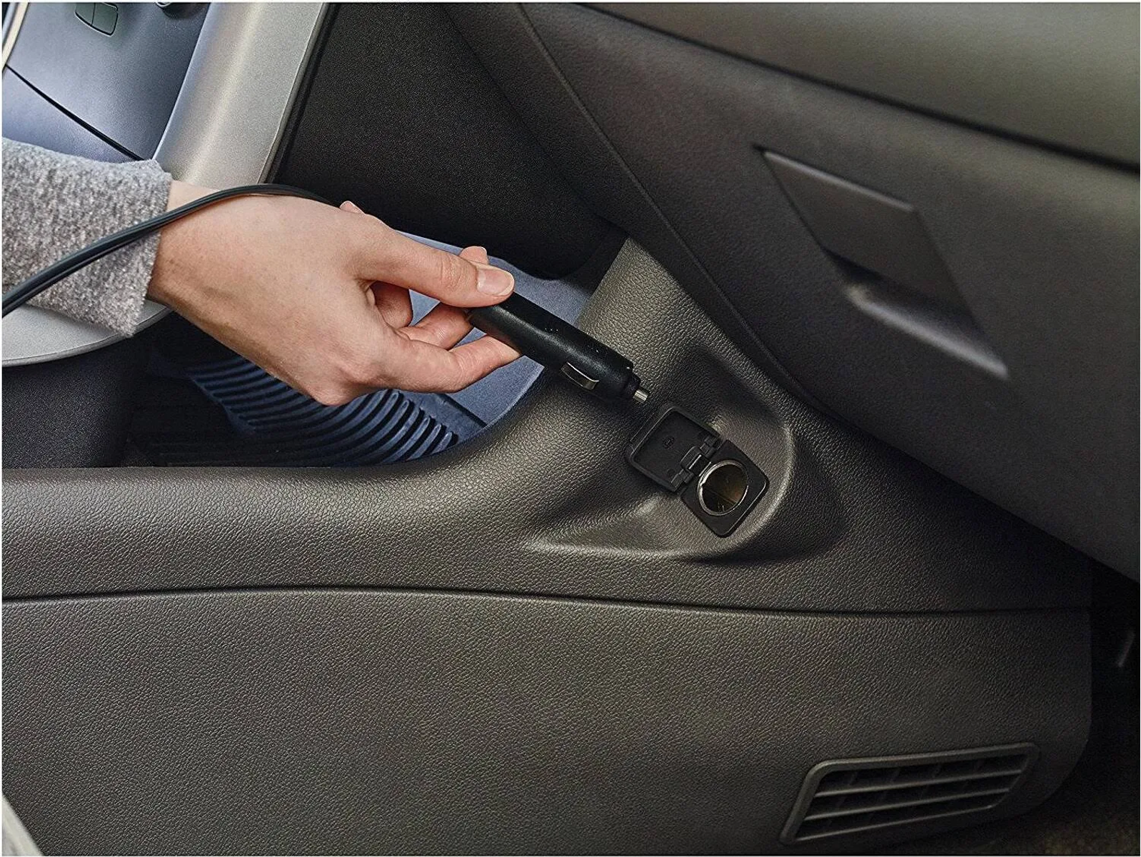 Hand steckt schwarzes Ladegerät in die Steckdose eines Autos.