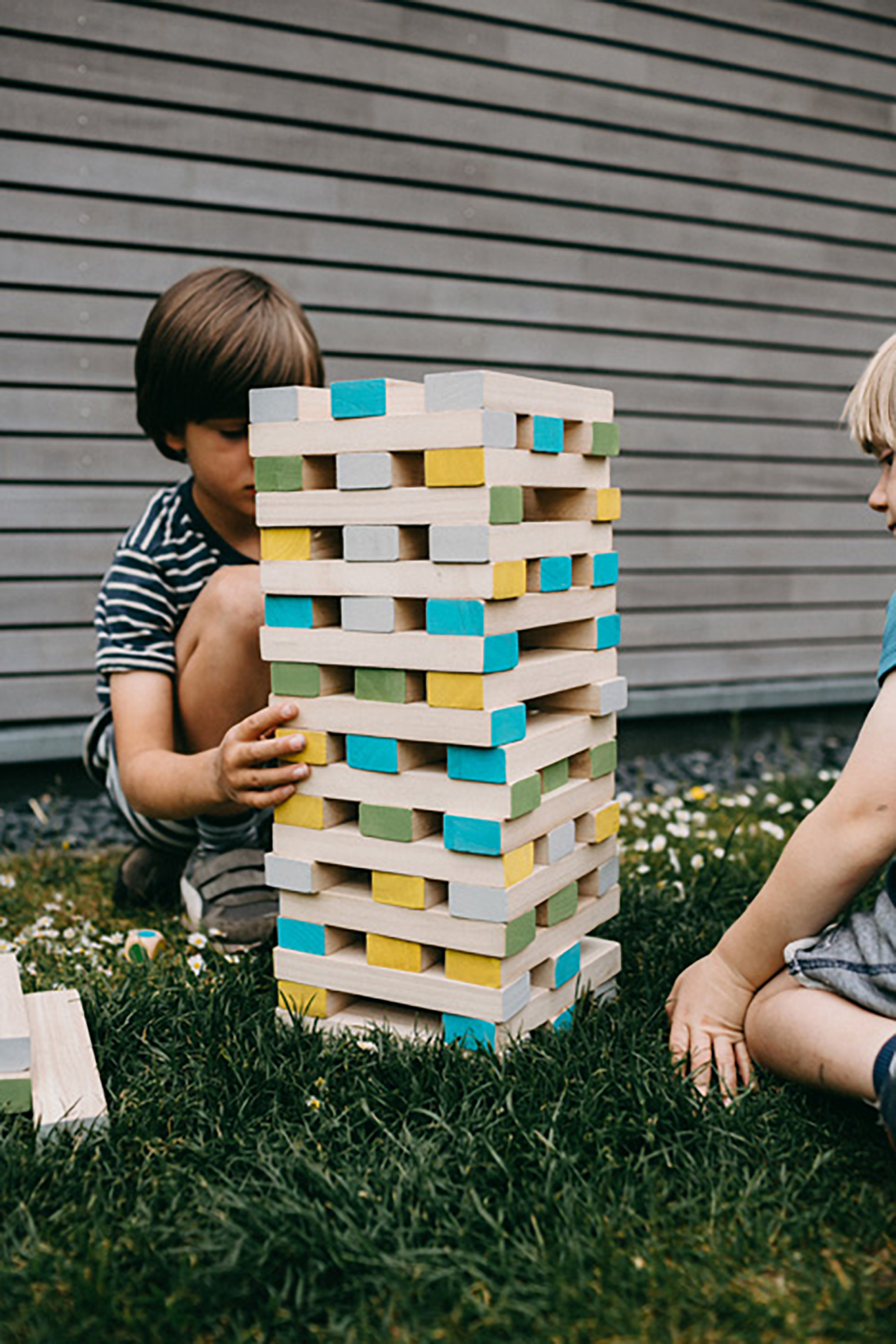 Zwei Jungen spielen ein Jenga-Turmspiel auf dem Gras. Die Blöcke sind farbig.