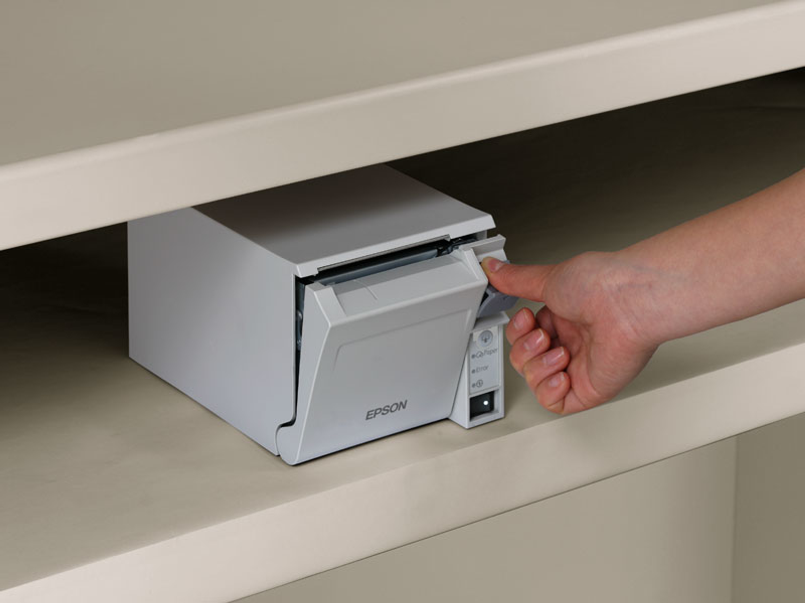 Une main tire du papier d'une imprimante Epson blanche à l'intérieur d'une étagère.