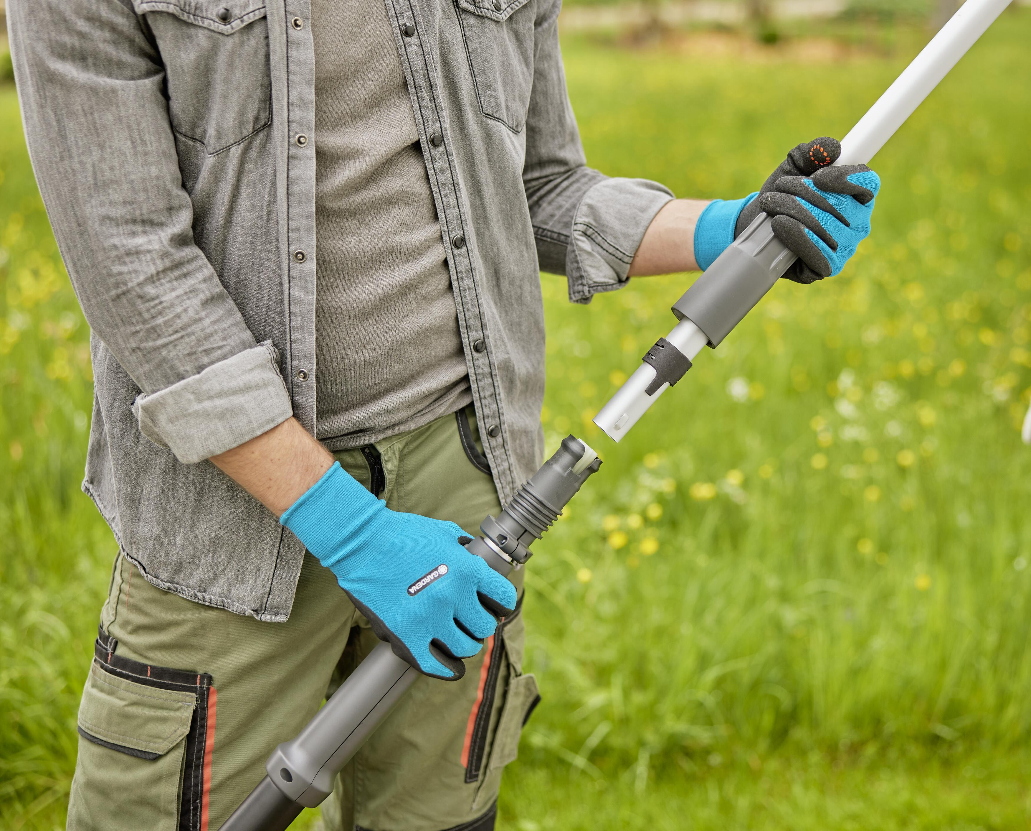 Person mit Handschuhen verbindet Teile einer Stange. Grünes Gras im Hintergrund.