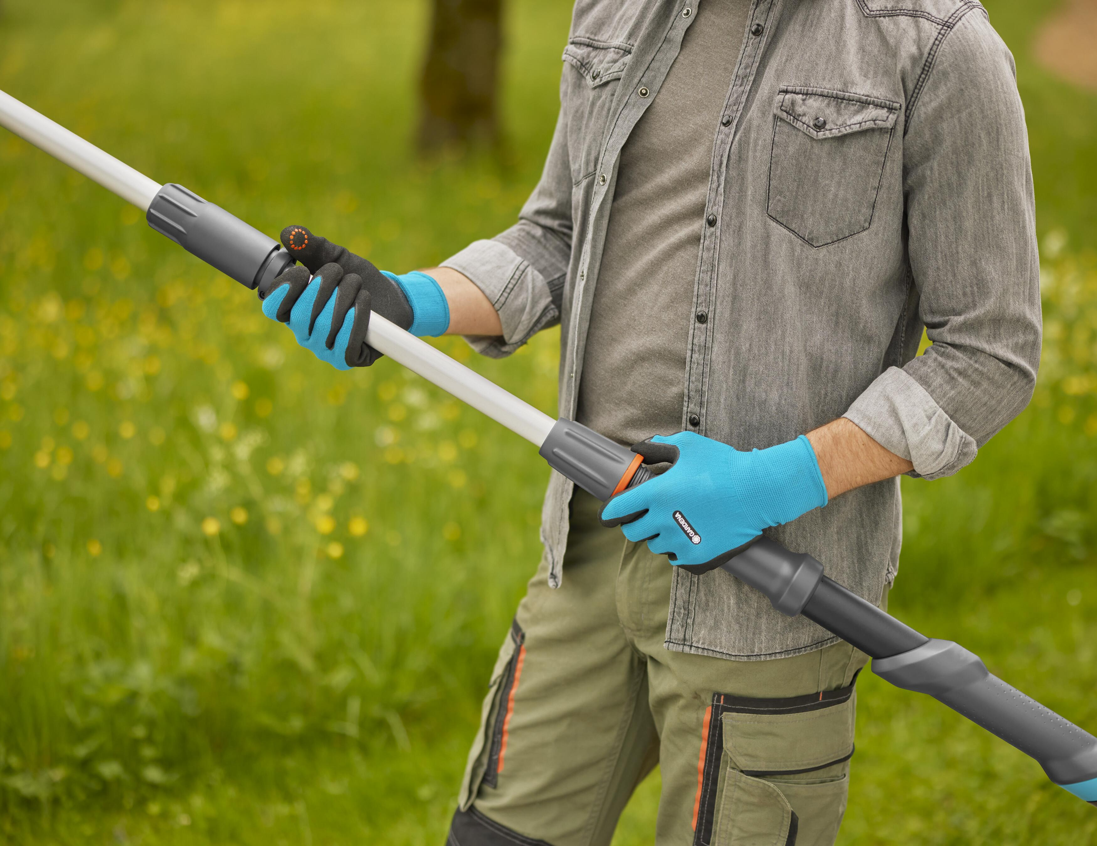 Eine Person mit Handschuhen hält ein Gartengerät in einer Gartenumgebung.