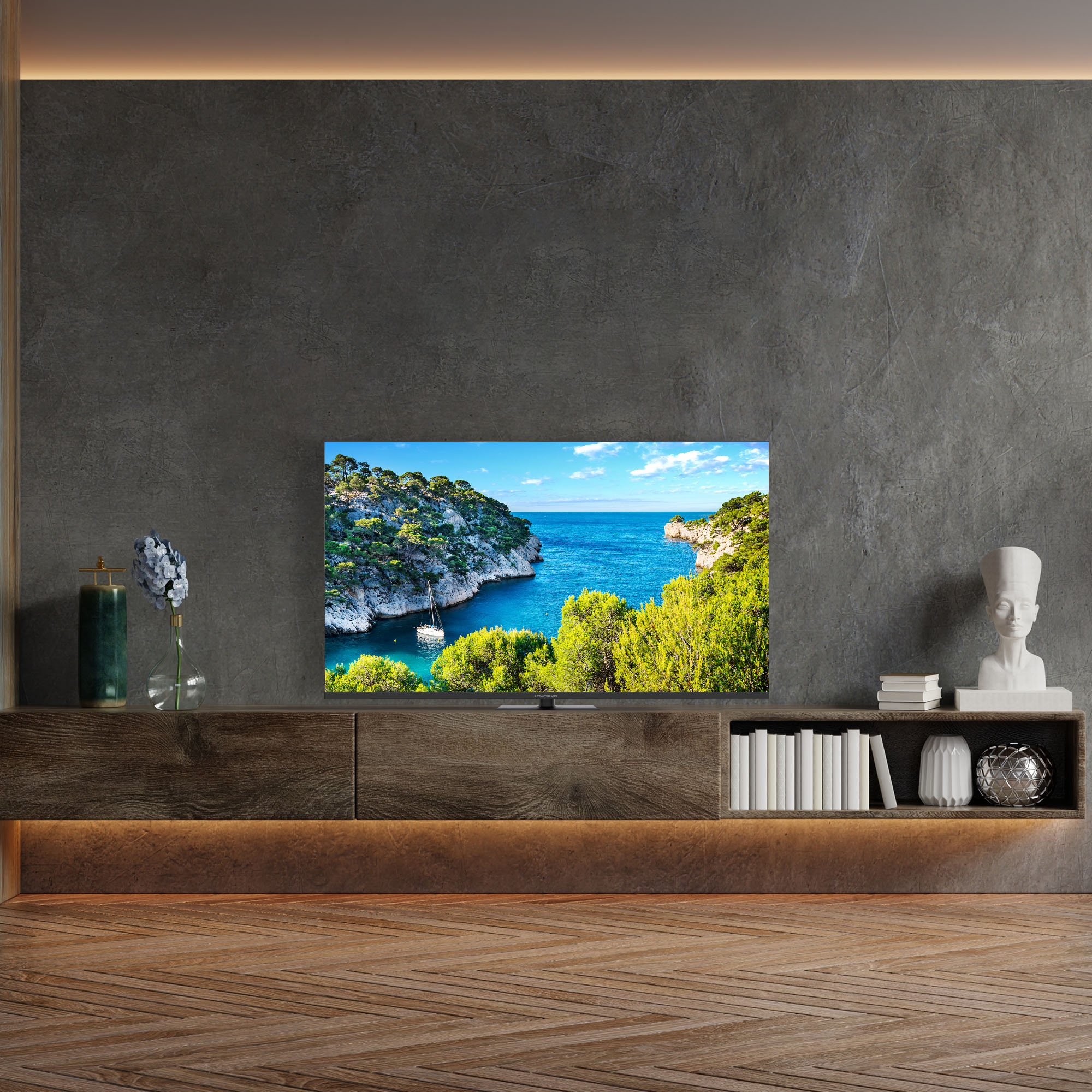 Telewizor wyświetlający scenę nadmorską, ustawiony na drewnianej szafce. Ciemnoszara ściana.