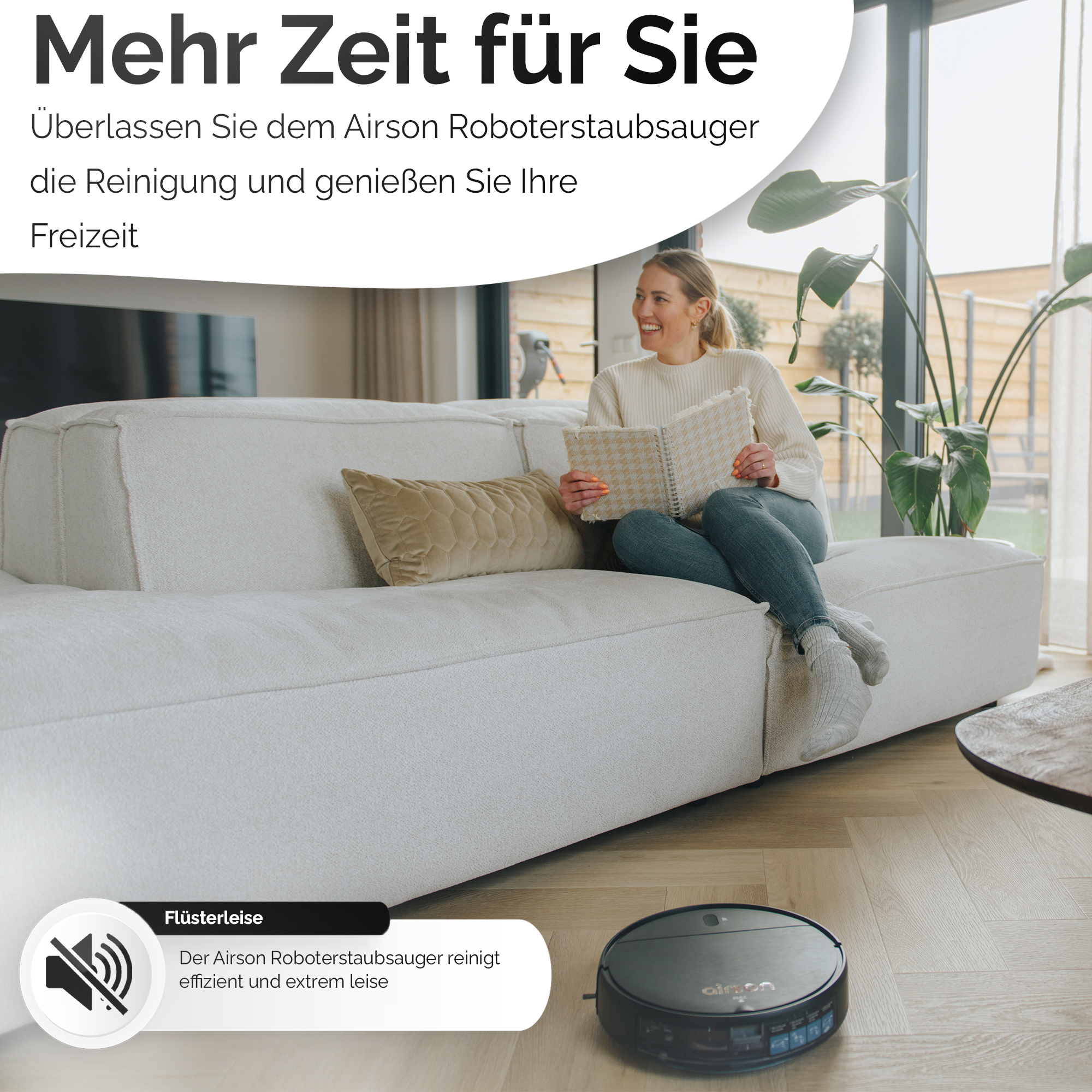 Eine Frau sitzt lesend auf einem Sofa, ein Roboter-Staubsauger auf dem Holzboden.