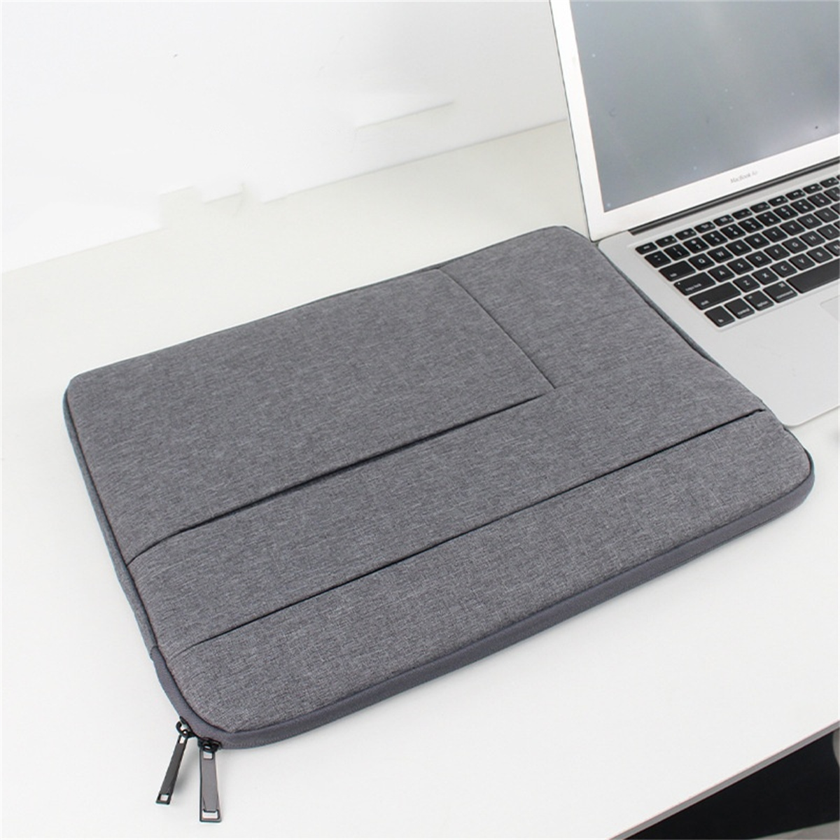 Eine graue Laptoptasche mit Reißverschluss und ein Laptop daneben auf einer weißen Oberfläche.
