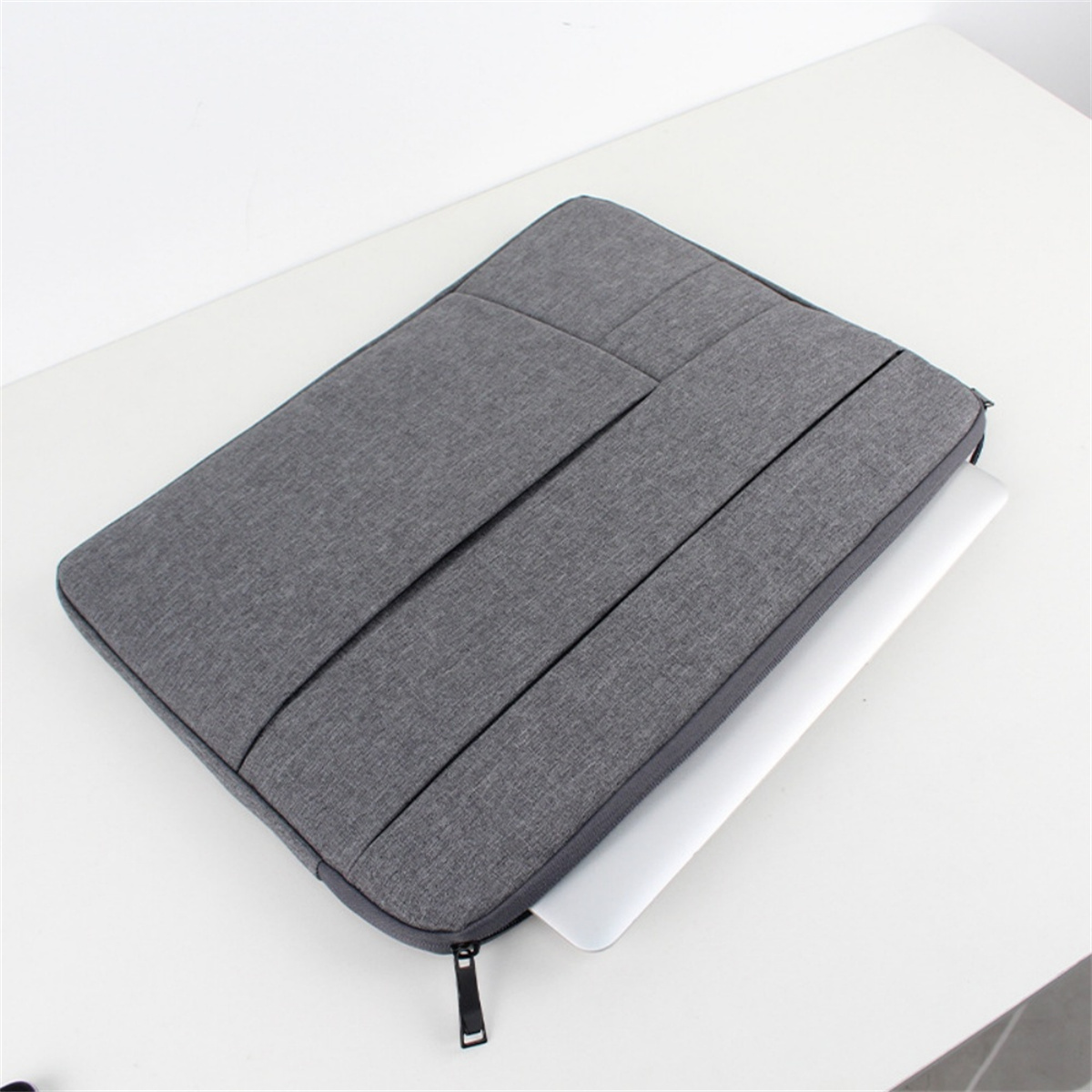 Ein grauer Laptop in einer grauen Laptoptasche auf einer weißen Oberfläche. Ein schwarzer Reißverschluss ist sichtbar.