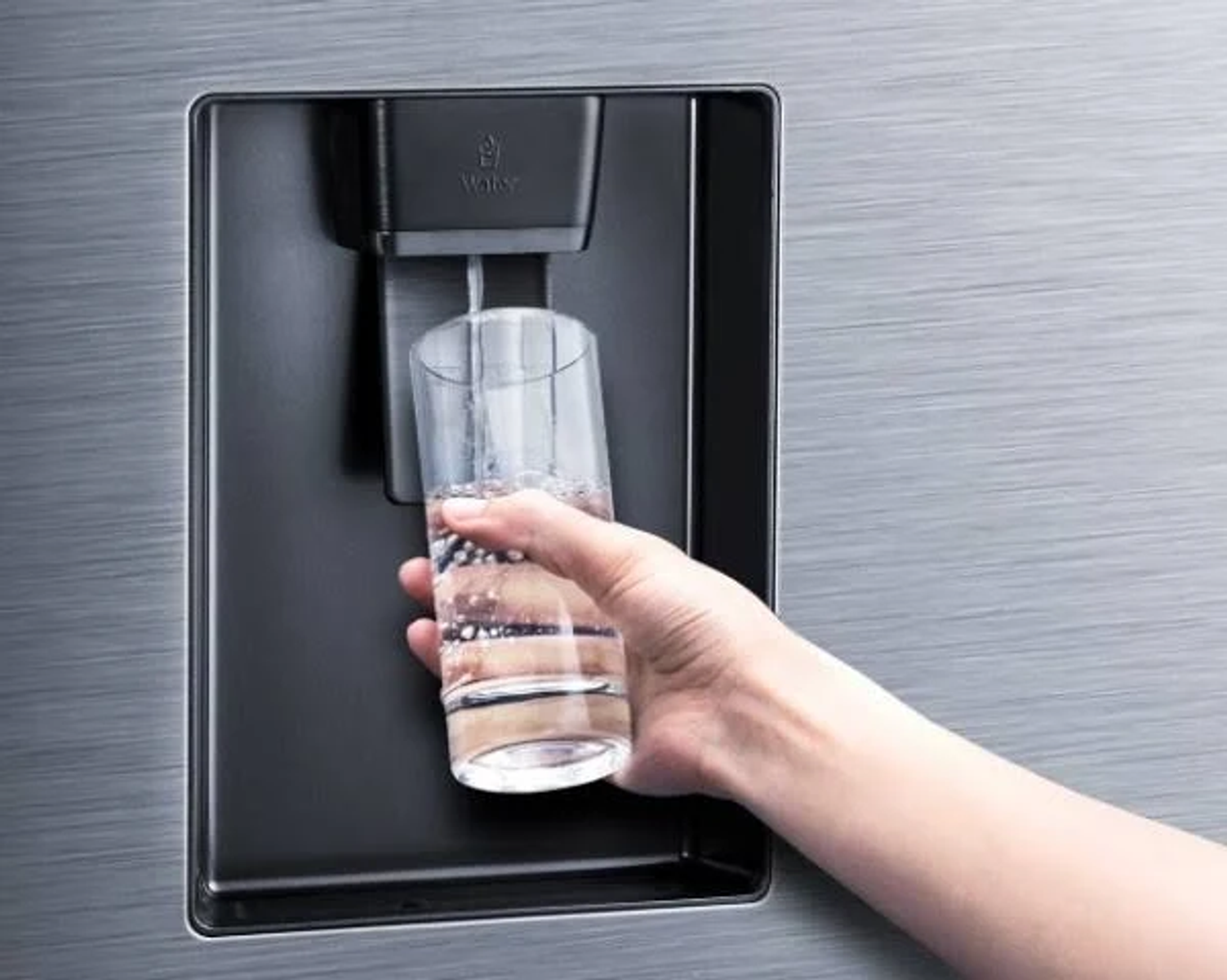 Una mano riempie un bicchiere con acqua da un distributore del frigorifero. Il frigorifero è in acciaio inox.