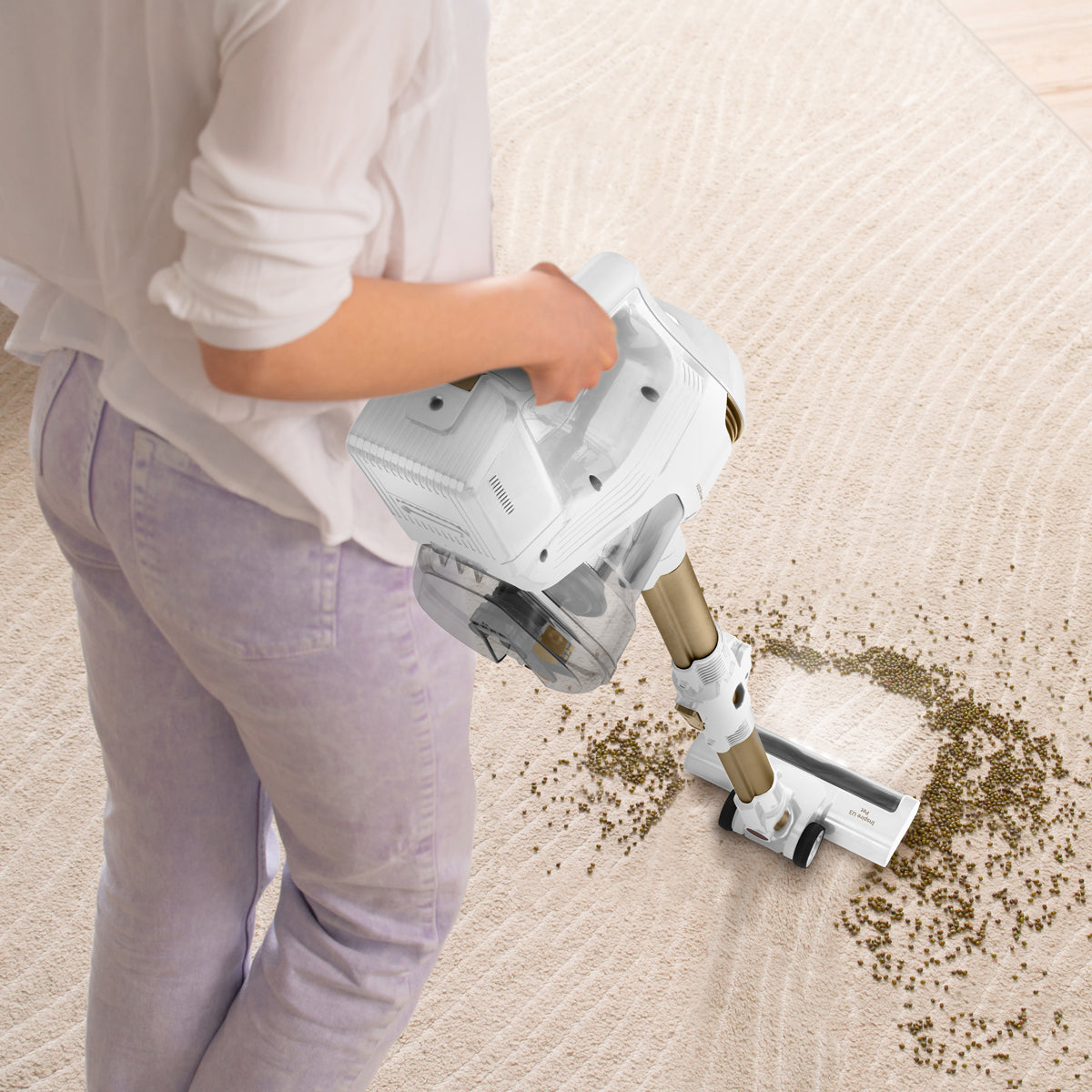 Una persona aspira una alfombra beige con una aspiradora blanca y dorada, recogiendo migas.