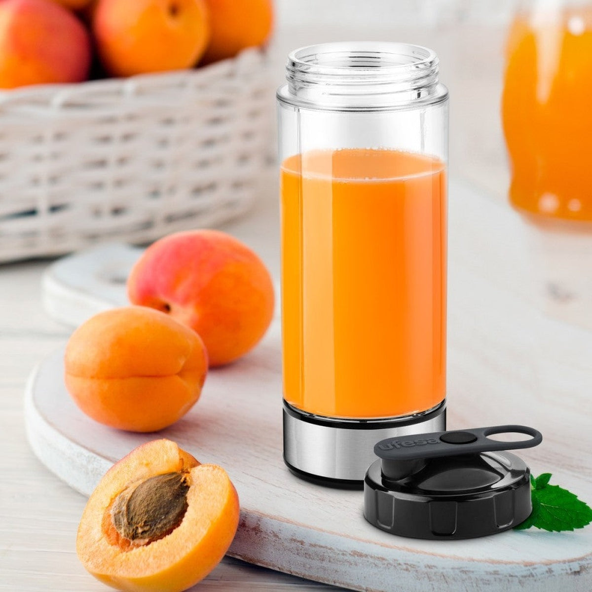 Un vaso de zumo de naranja con tapa negra, junto a albaricoques sobre una tabla de madera.