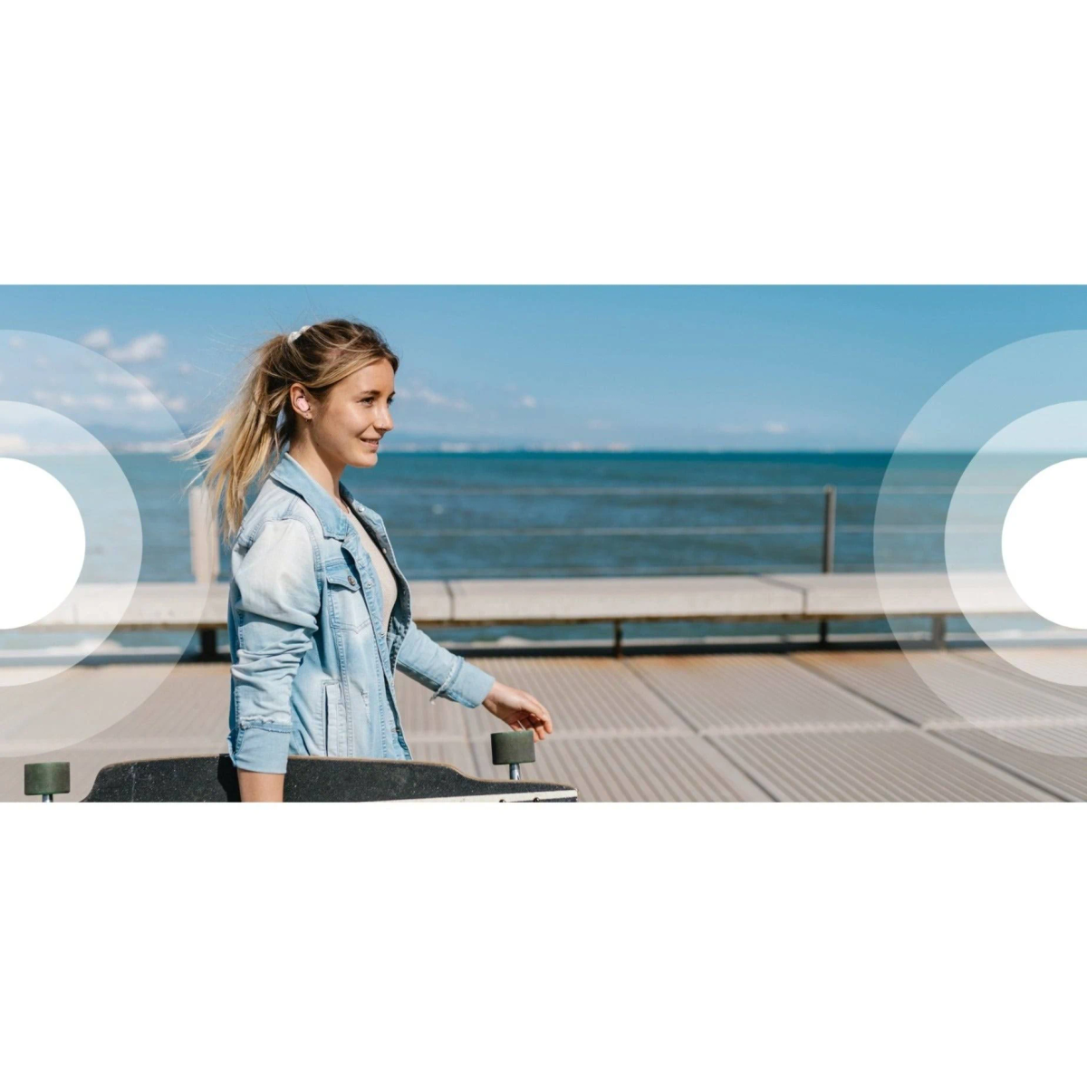 Una mujer con cabello rubio caminando en un muelle con una patineta.