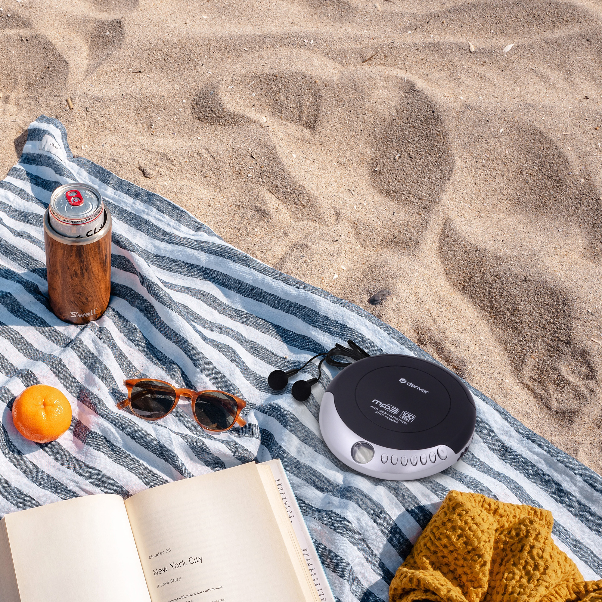 Scena na plaży z odtwarzaczem CD, książką, okularami przeciwsłonecznymi i puszką sody na ręczniku.