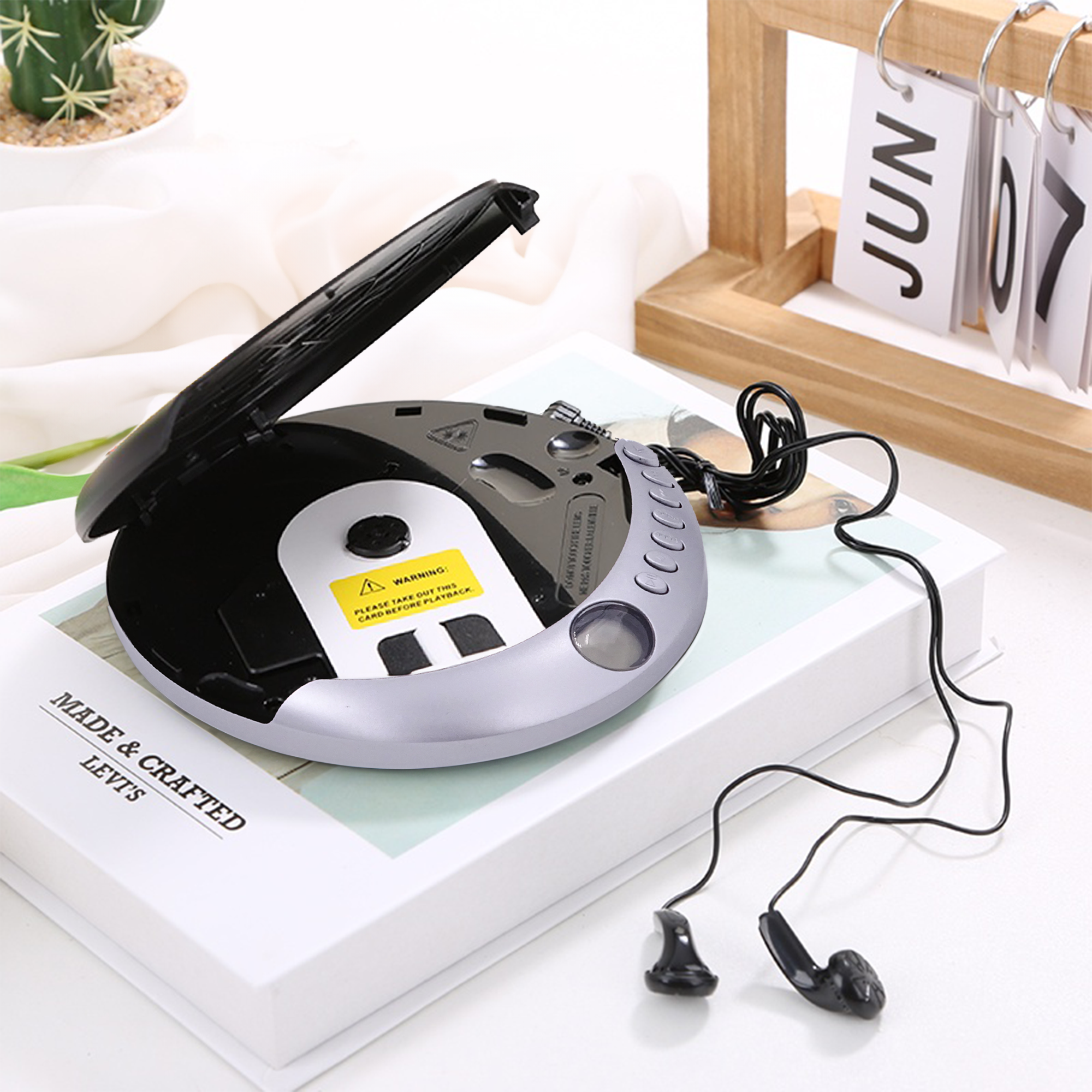 Przenośny odtwarzacz CD, otwarty, ze słuchawkami leżącymi na książce z kalendarzem z tyłu.