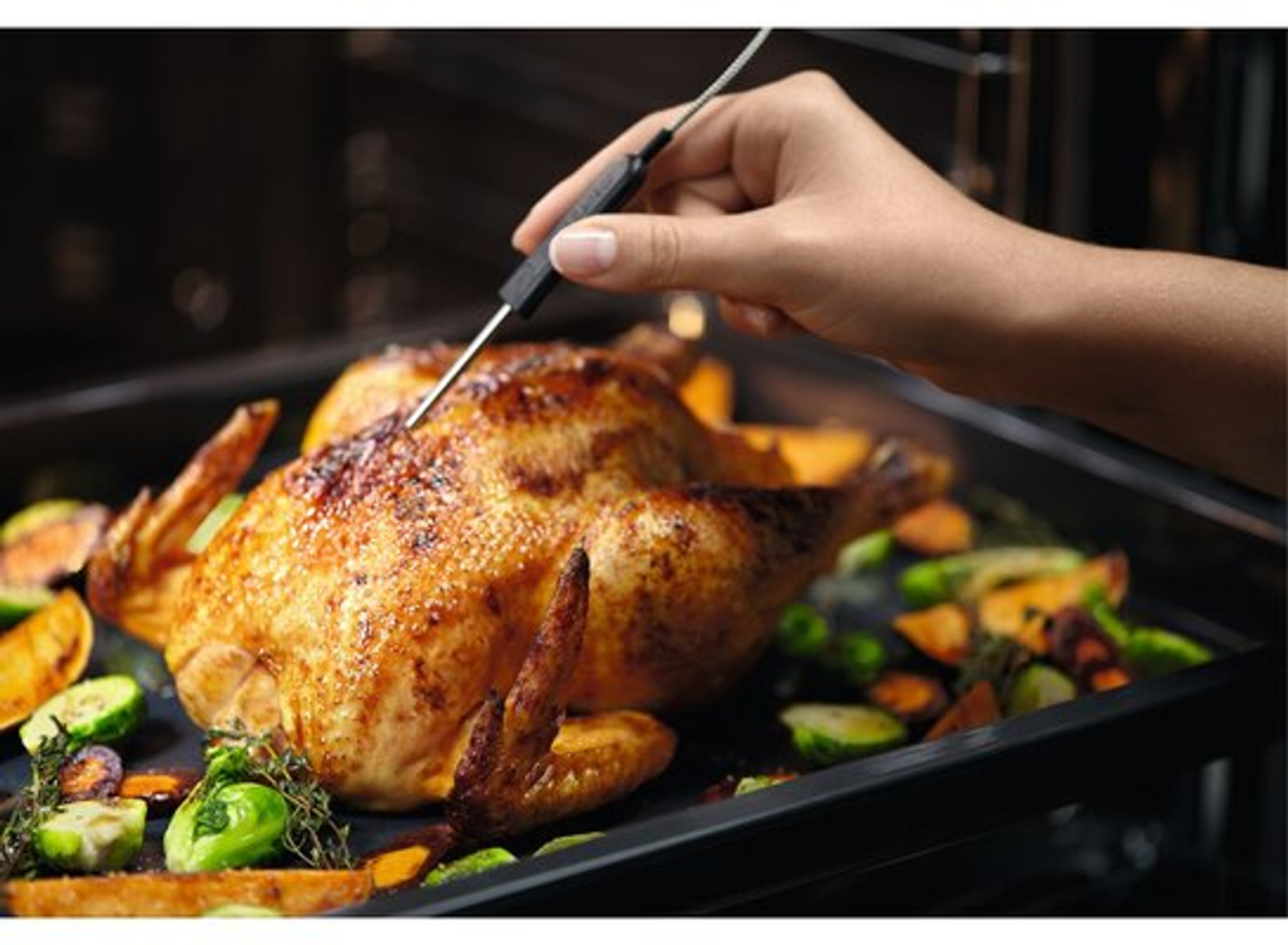 Osoba używająca termometru do sprawdzenia temperatury pieczonego kurczaka na patelni.