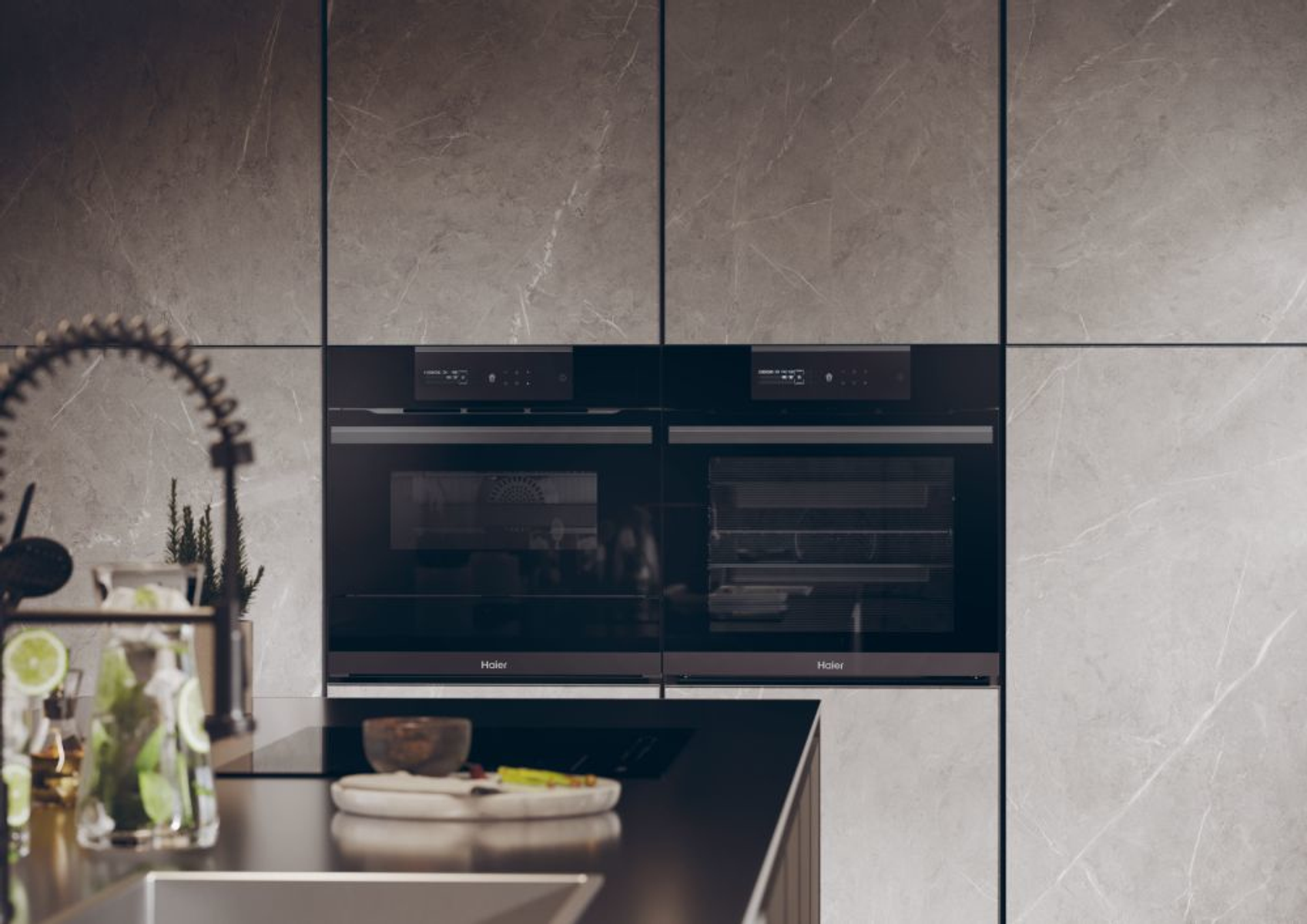 Cucina moderna con due forni neri a incasso, pareti in marmo e primo piano sfocato.