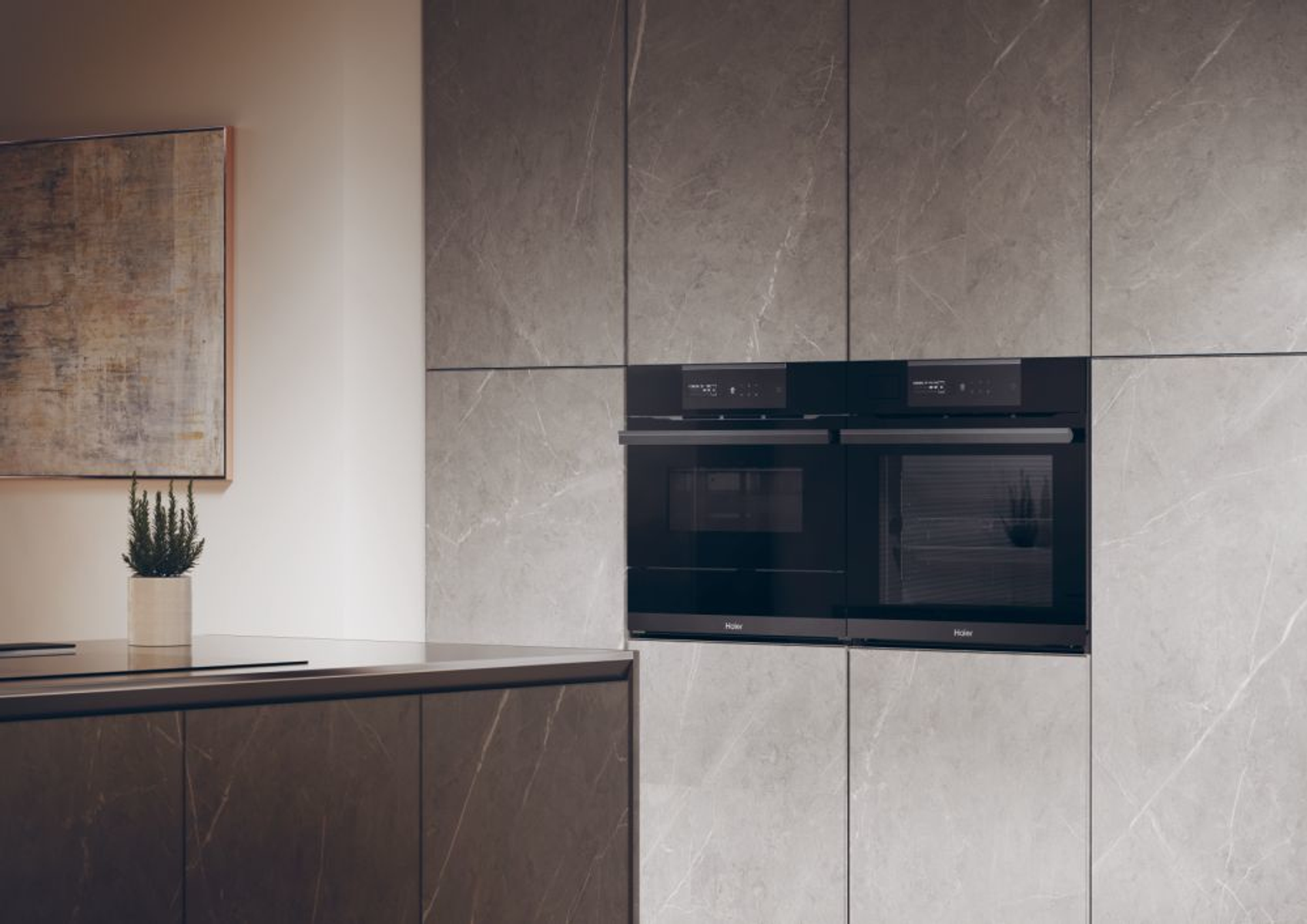 Cucina moderna con forni neri a incasso e mobili grigi effetto marmo.