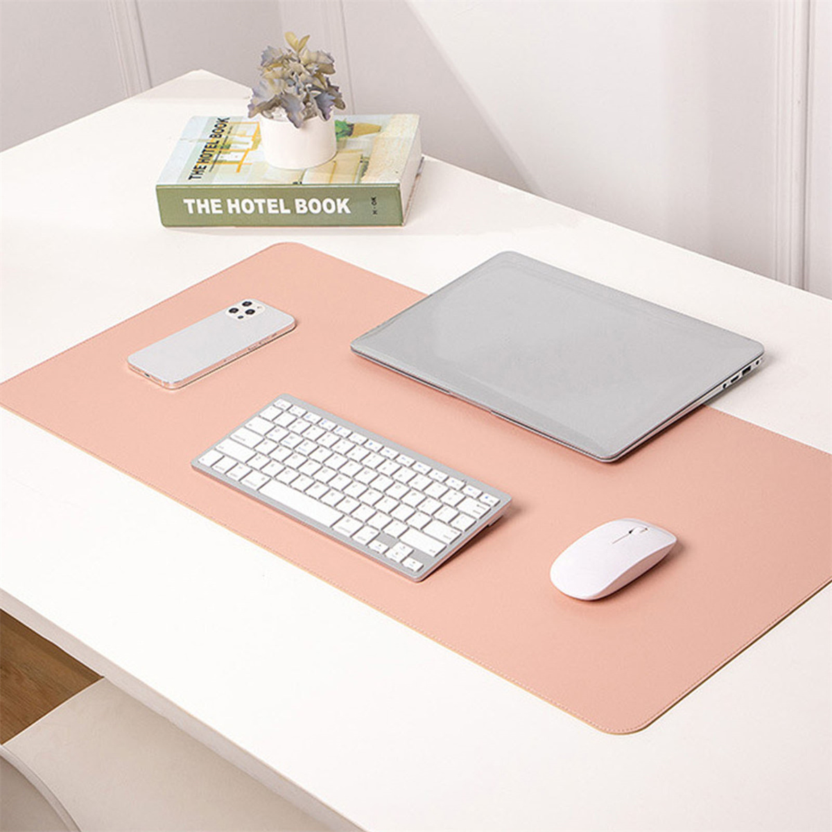 Schreibtisch mit rosa Matte, Laptop, Telefon, Tastatur und Maus.