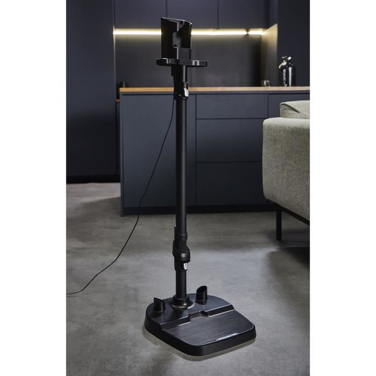 Czarny stojak na odkurzacz na szarej podłodze z kuchnią w tle.