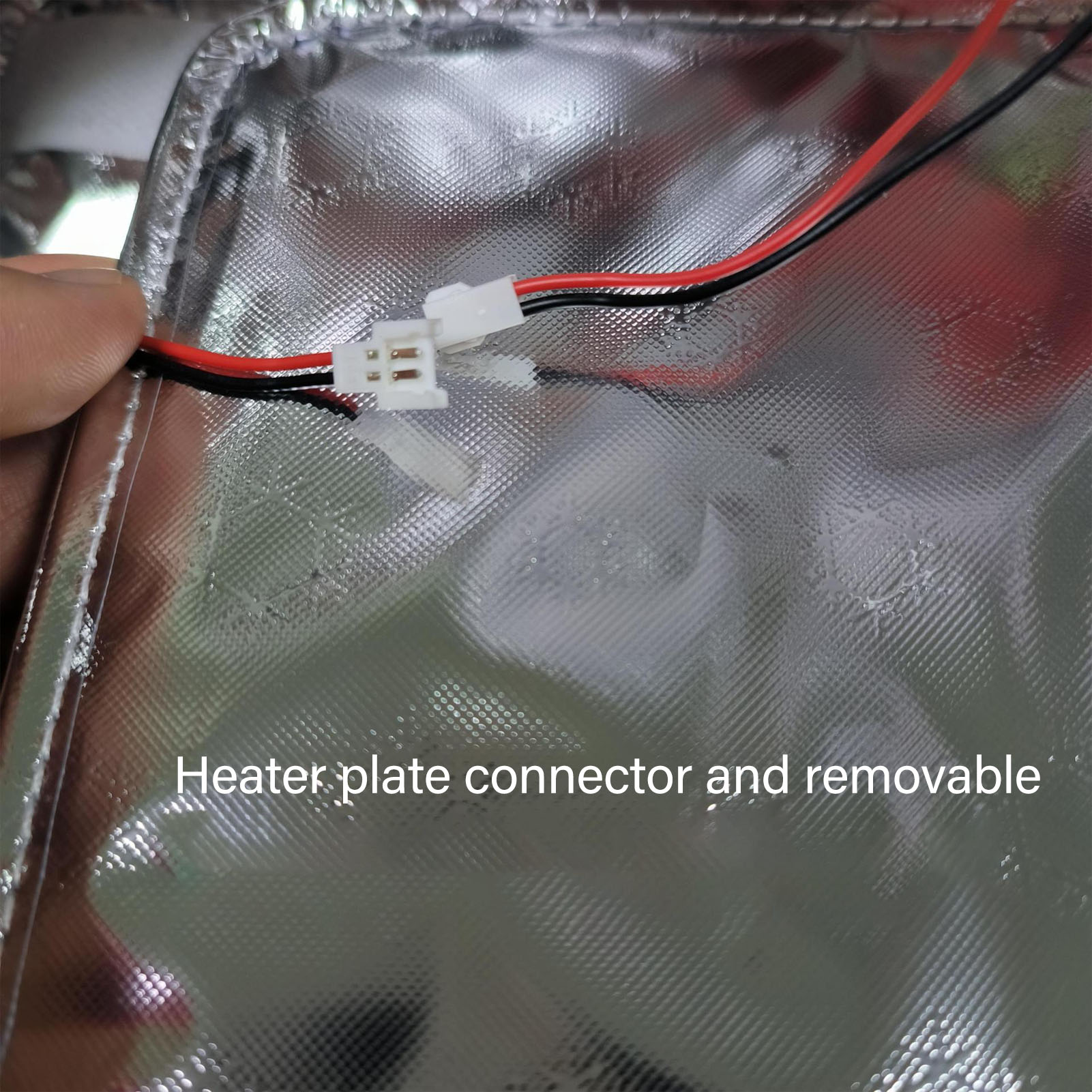 Nahaufnahme eines silbernen Heizplattenanschlusses, schwarze und rote Drähte, weißer Stecker.
