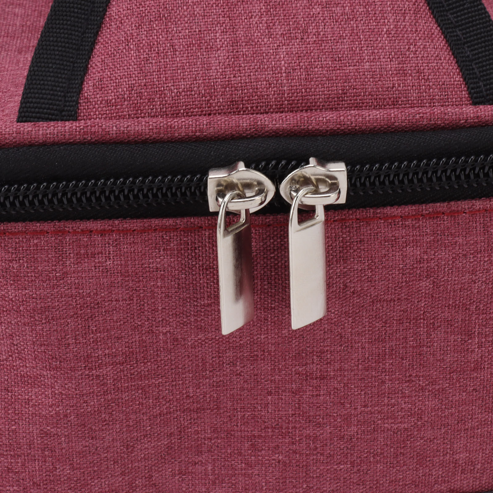 Nahaufnahme einer weinroten Lunchtasche. Zwei silberne Reißverschlüsse sind sichtbar.