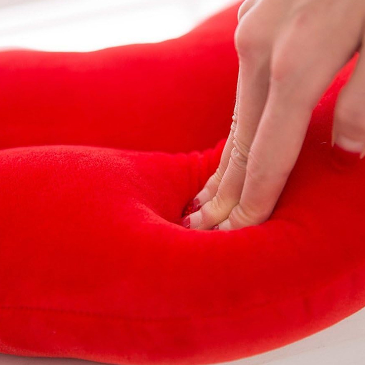 Eine Hand drückt in ein rotes Kissen und zeigt die Vertiefung.