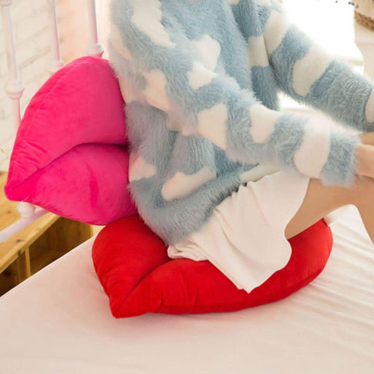 Eine Person sitzt auf einem roten und pinkfarbenen kissenförmigen Lippen, trägt einen blauen Pullover.