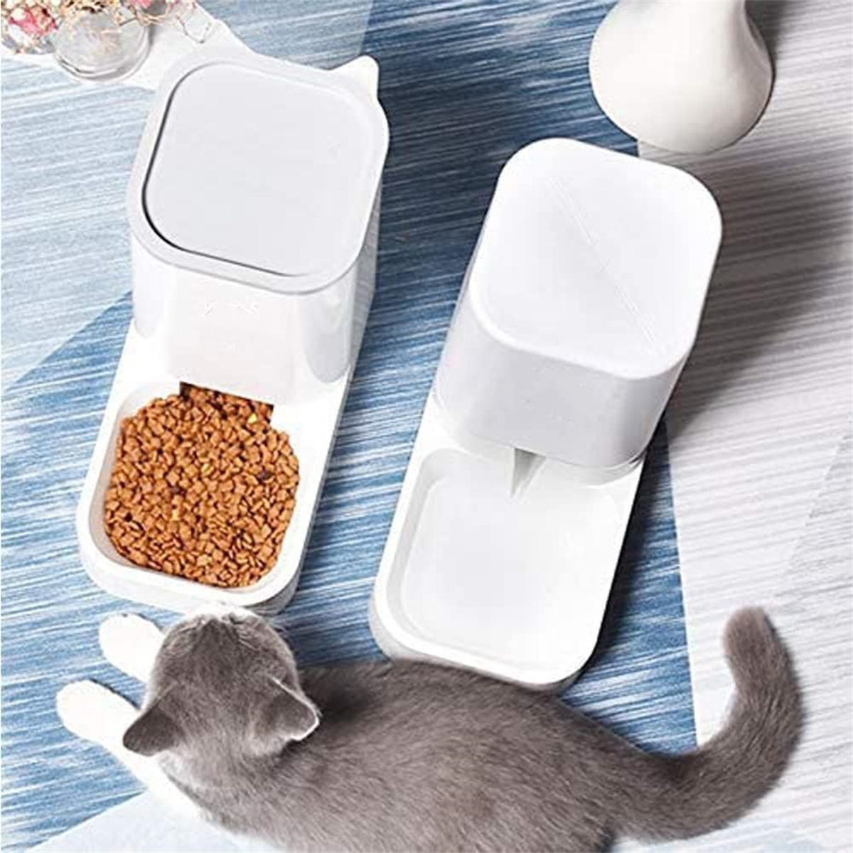 Weißer Katzenfutterspender mit Futter- und Wasserfächern und eine graue Katze, die sich hinlegt.