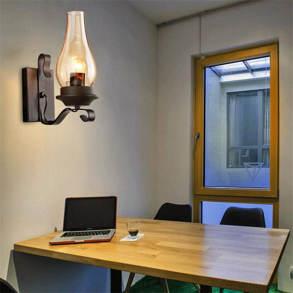 Eine Wandlampe mit bernsteinfarbenem Glasschirm, einem Laptop und einer Tasse auf einem Tisch.