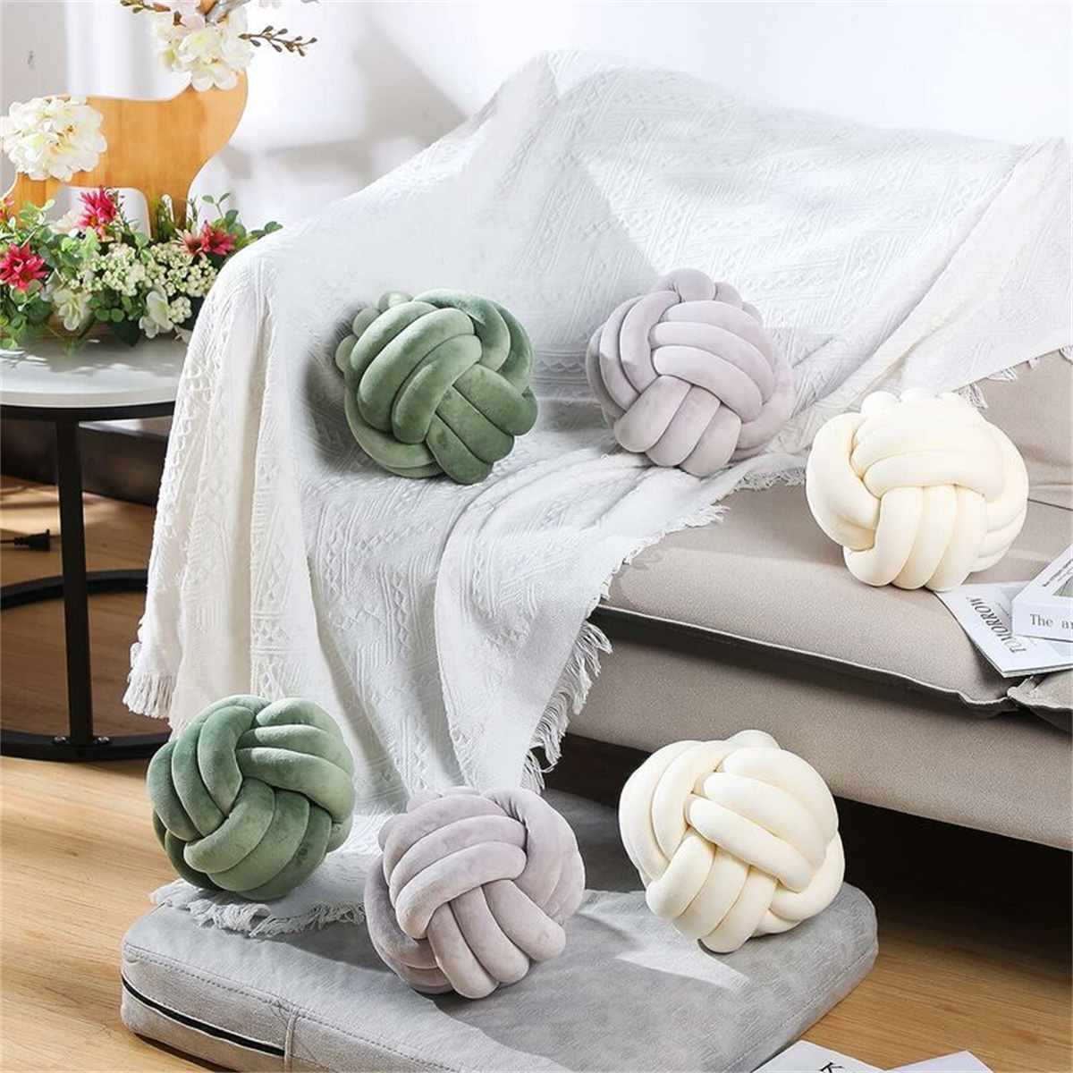 Knotenförmige Kissen in verschiedenen Farben auf einem Sofa und einem Hocker. Sie sind in Grün, Grau und Off-White.