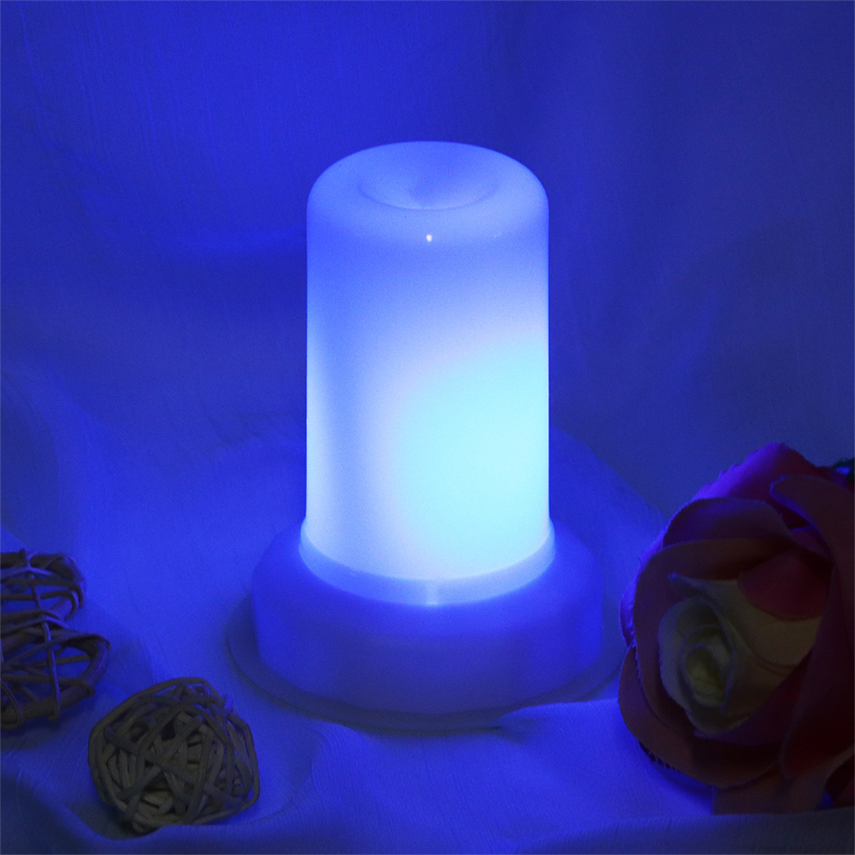 Eine blau beleuchtete, zylindrische Lampe. Eine Rose und ein geflochtener Ball sind in der Nähe.