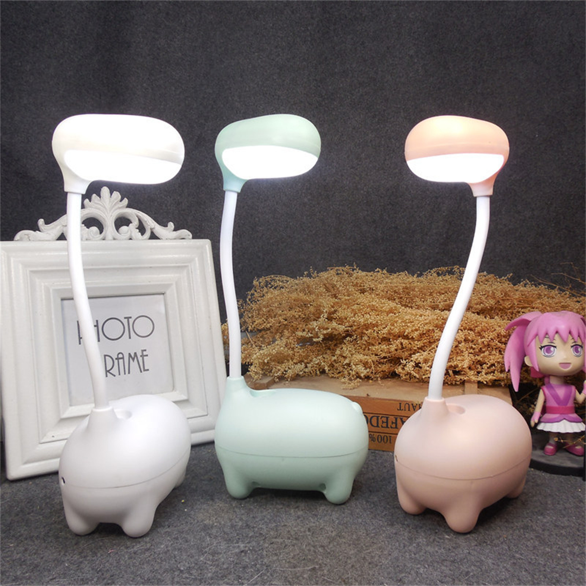 Drei niedliche Lampen mit Tierform-Basis. Lampen sind weiß, grün und rosa. Ein Bilderrahmen und der Hintergrund ist grau.