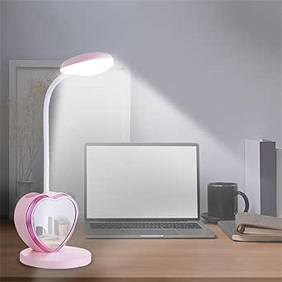 Eine pinkfarbene, herzförmige Schreibtischlampe mit weißem Licht, auf einem Holztisch mit Laptop und Tasse.