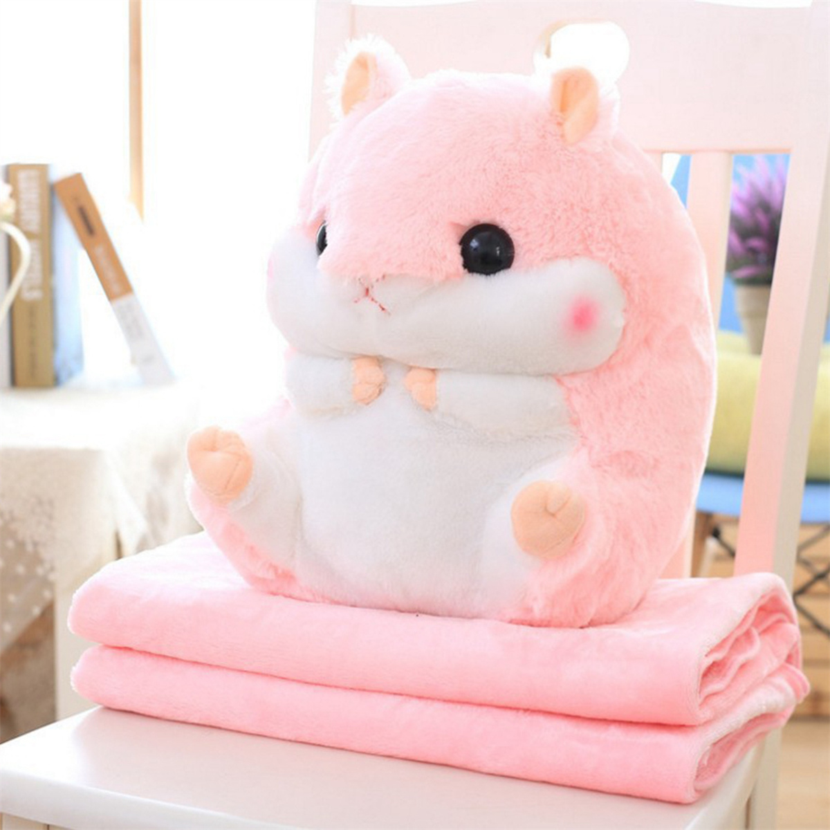 Rosa Plüsch-Hamster-Spielzeug sitzt auf einer rosa Decke, platziert auf einem weißen Stuhl, Hintergrund ist ein Fenster.