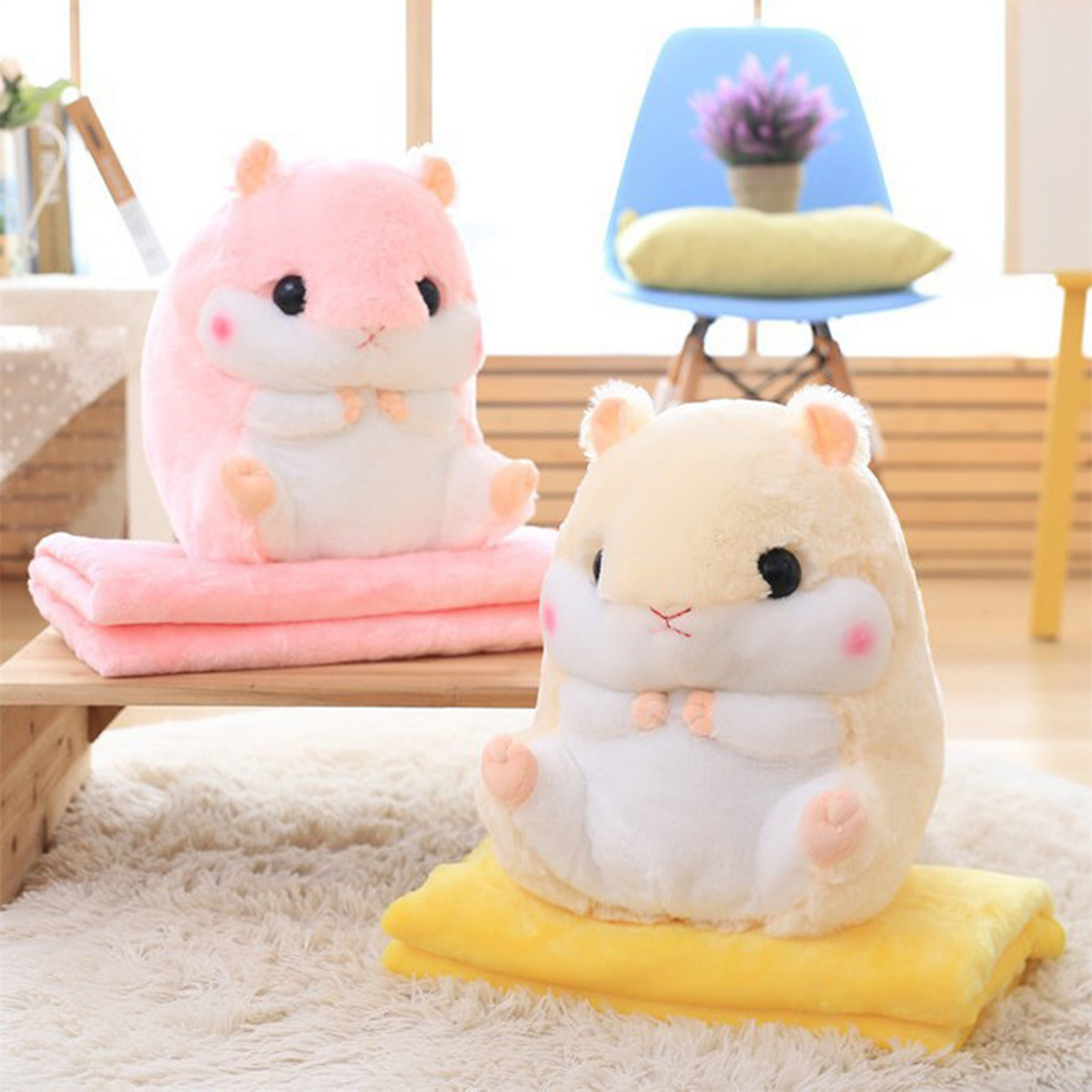 Zwei Plüsch-Hamster-Spielzeuge auf rosa und gelben Decken. Ein blauer Stuhl im Hintergrund.